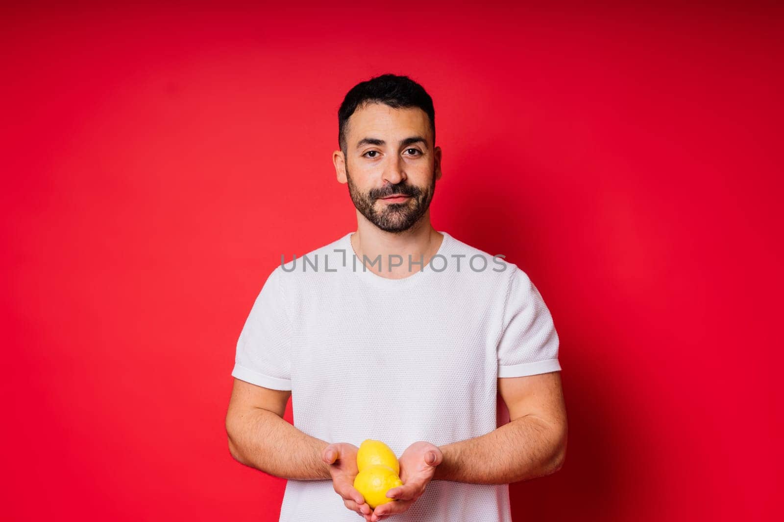 Portrait of young bearded man holding lemons in both hands on an isolated red background