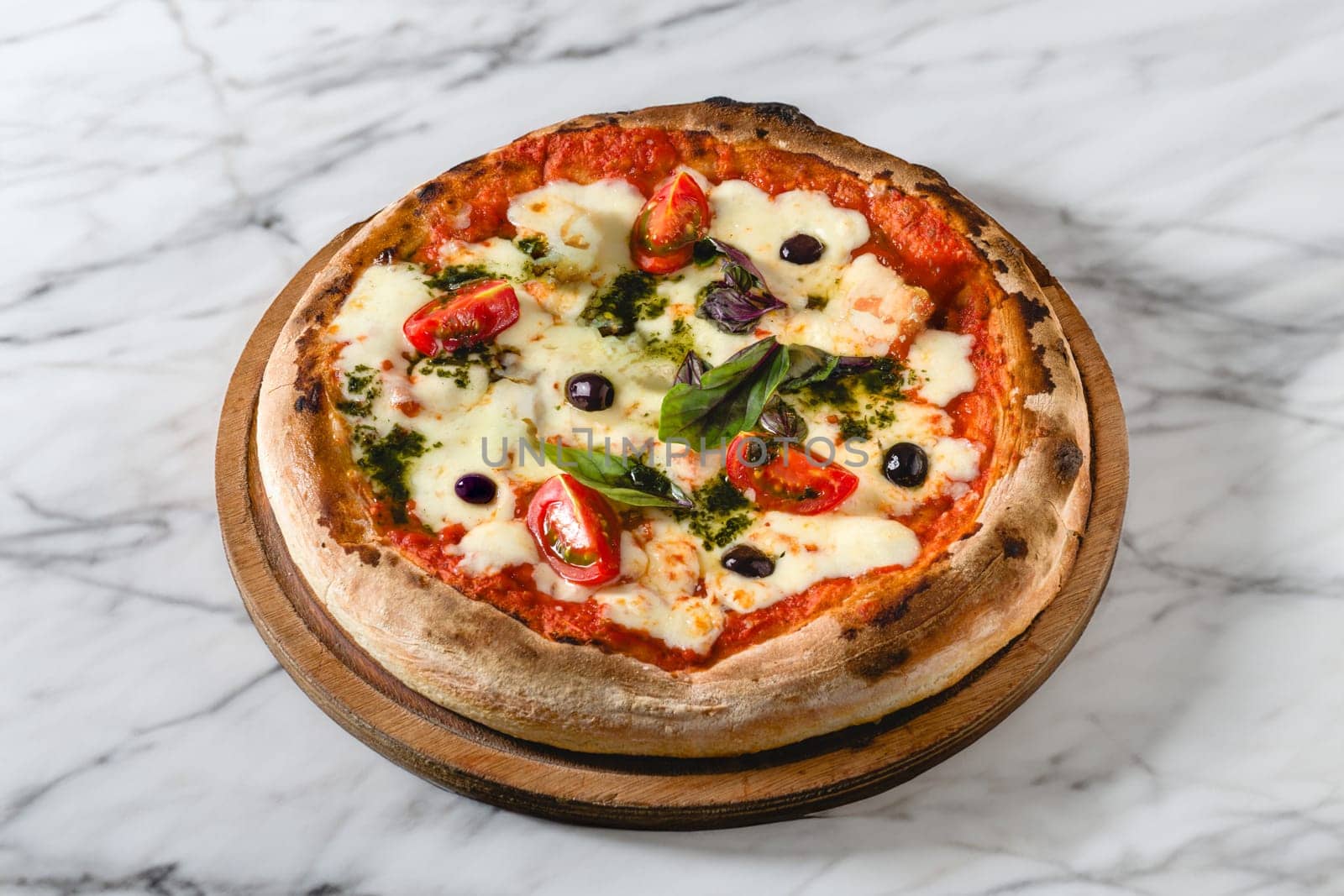 Neapolitan pizza with tomatoes, mozzarella, basil and olives on marble table