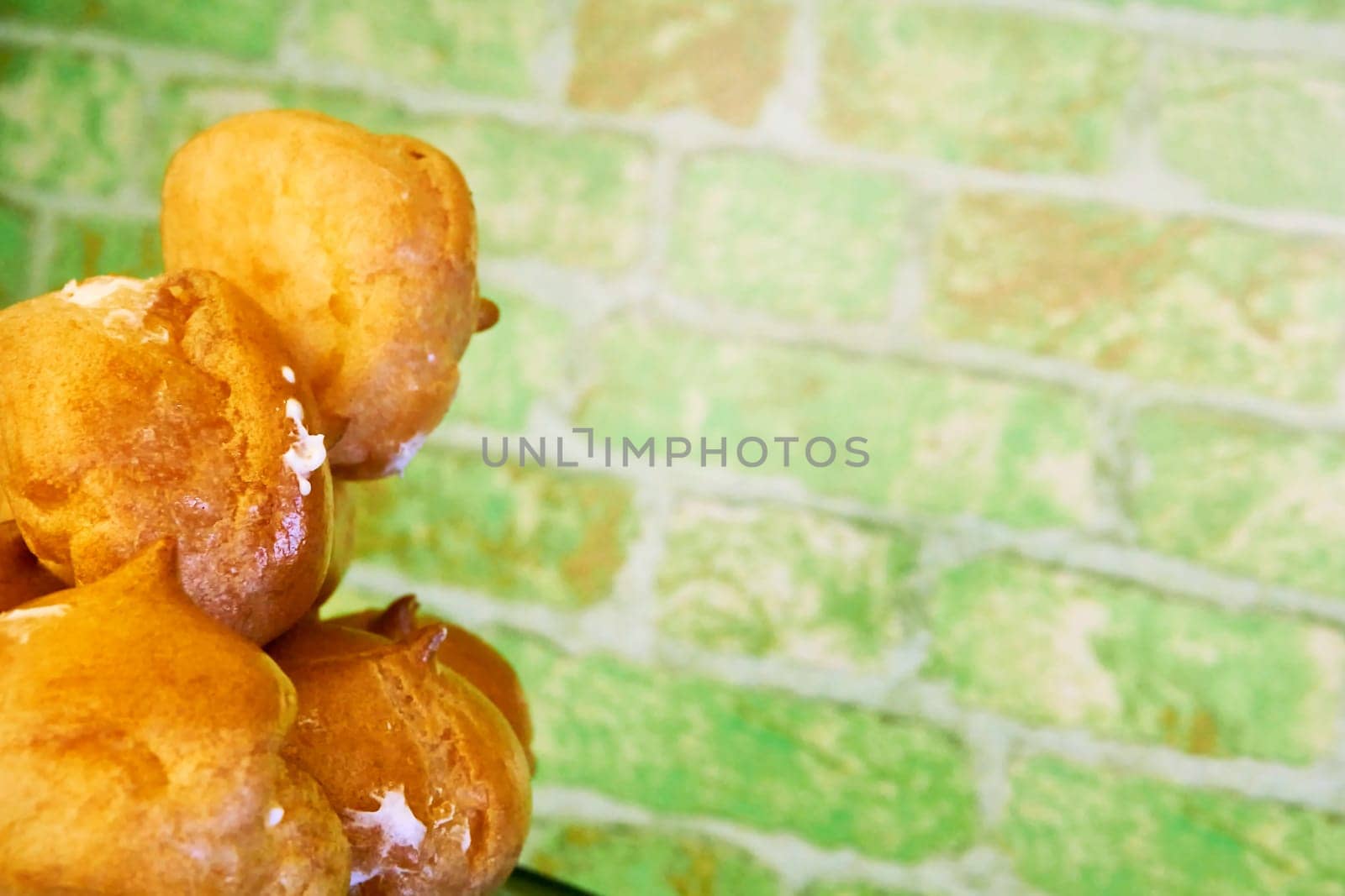 Delicious baked cakes profiteroles with cream.Green brick wall by jovani68