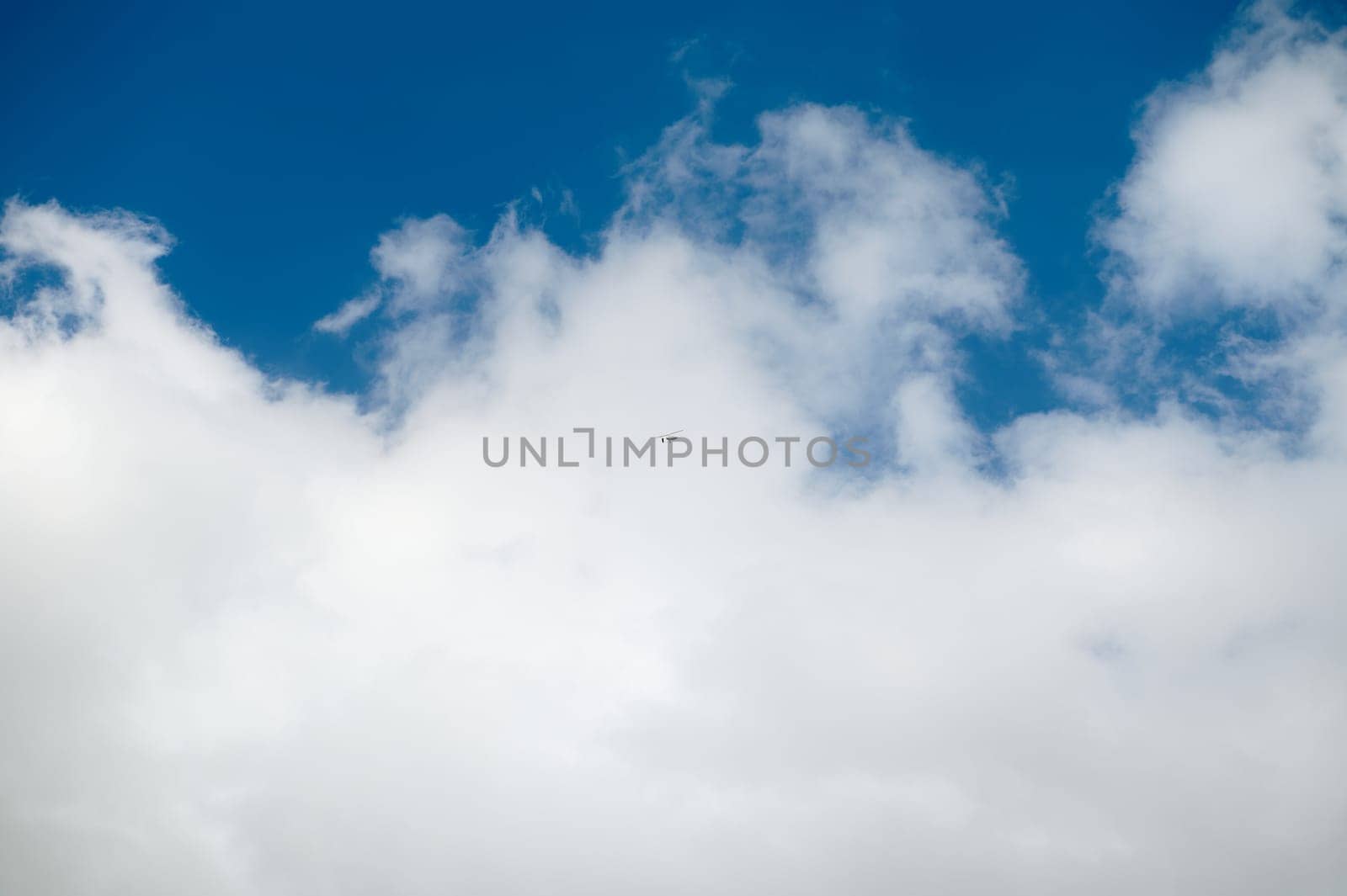 A small airplane flying high in the clear blue sky surrounded by fluffy white clouds. A serene and peaceful scene depicting freedom and travel.