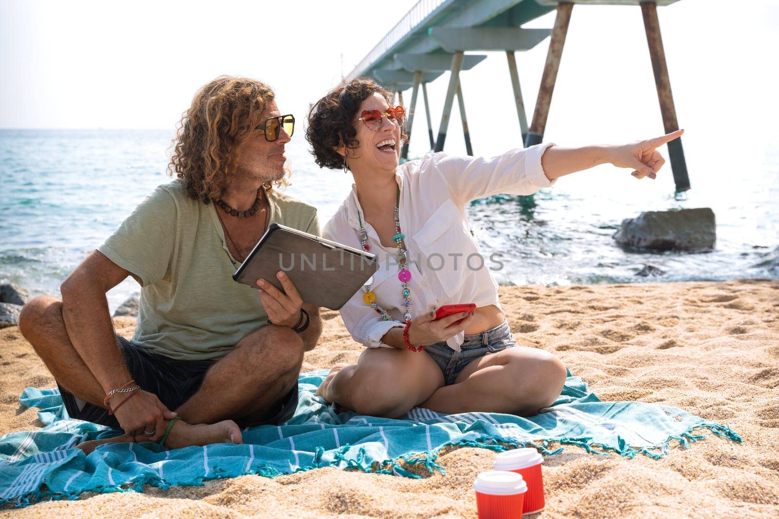 Couple on the beach,pointing to the location of the hotel with the tablet by mariaphoto3