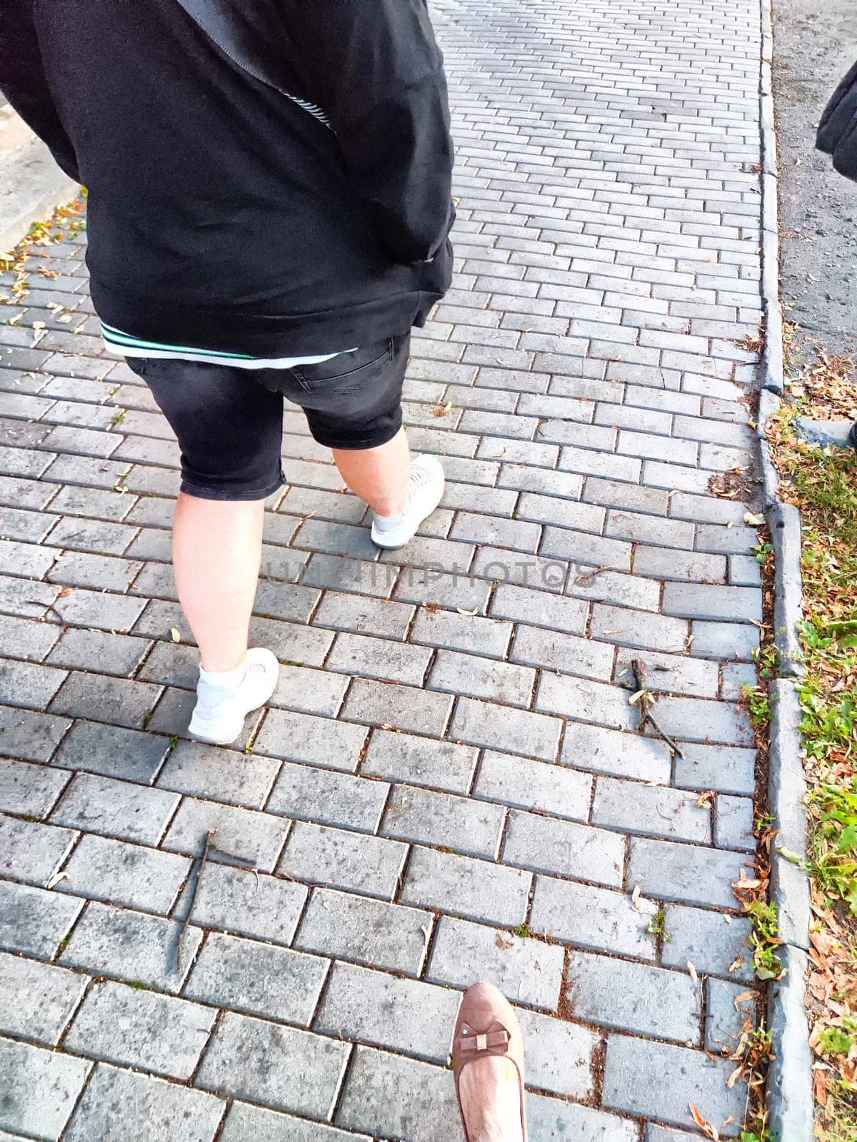 Person walking on brick-laid path in the evening. Casual Stroll on Cobblestone Sidewalk at Dusk