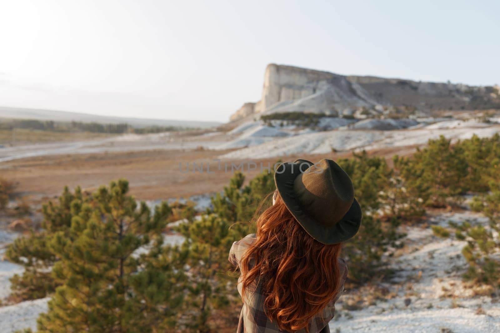 Redhaired woman in hat gazes at majestic mountain vista on horizon