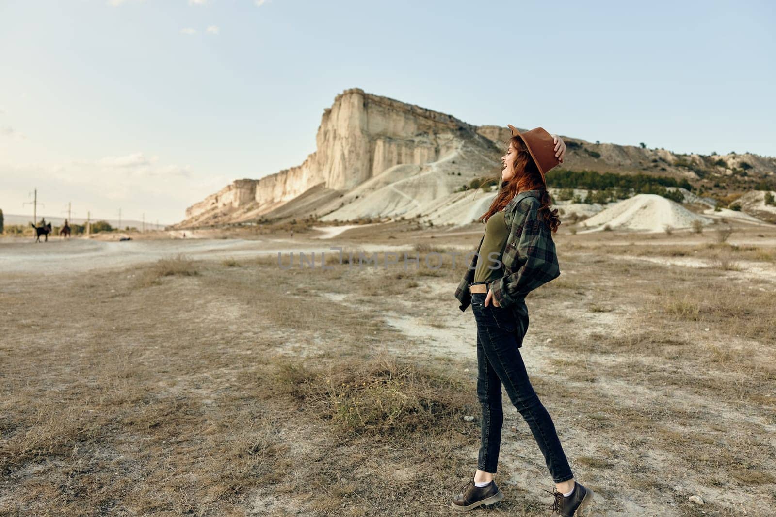 Woman in jeans and hat standing confidently in front of majestic mountain range by Vichizh