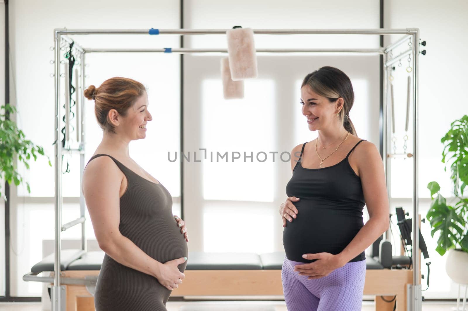 Two pregnant women communicate in a fitness club. Pilates for expectant mothers