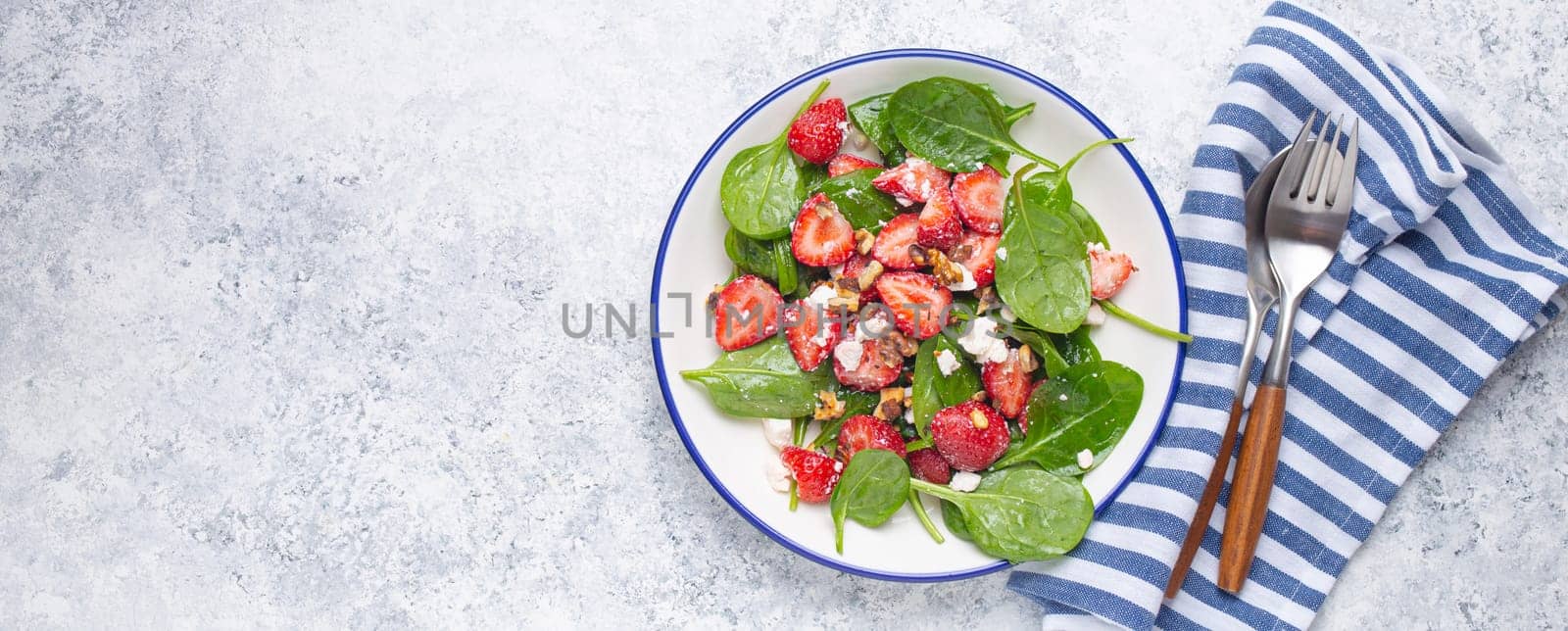 Light Healthy Summer Salad with fresh Strawberries, Spinach, Cream Cheese and Walnuts on White Ceramic Plate, white rustic stone Background From Above, Space For Text.