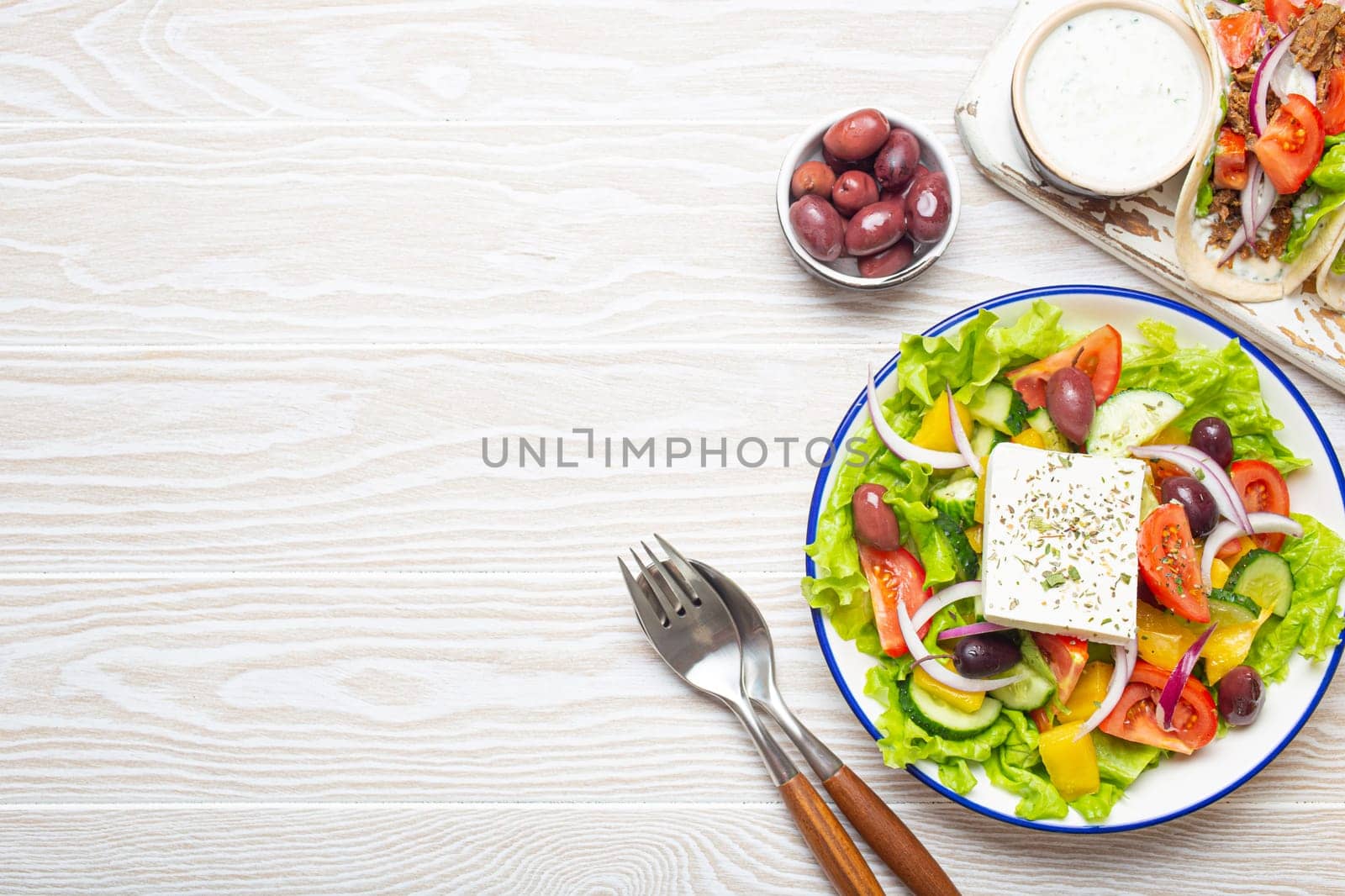 Traditional Greek Food: Greek Salad, Gyros with meat and vegetables, Tzatziki sauce, Olives on White rustic wooden table background from above. Cuisine of Greece. Copy space