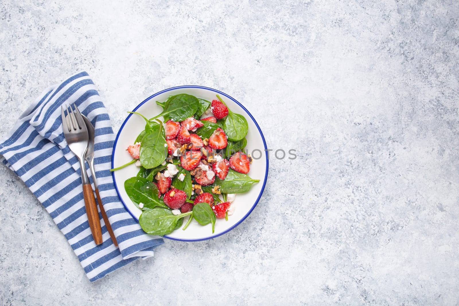 Light Healthy Summer Salad with fresh Strawberries, Spinach, Cream Cheese and Walnuts on White Ceramic Plate, white rustic stone Background From Above, Space For Text.