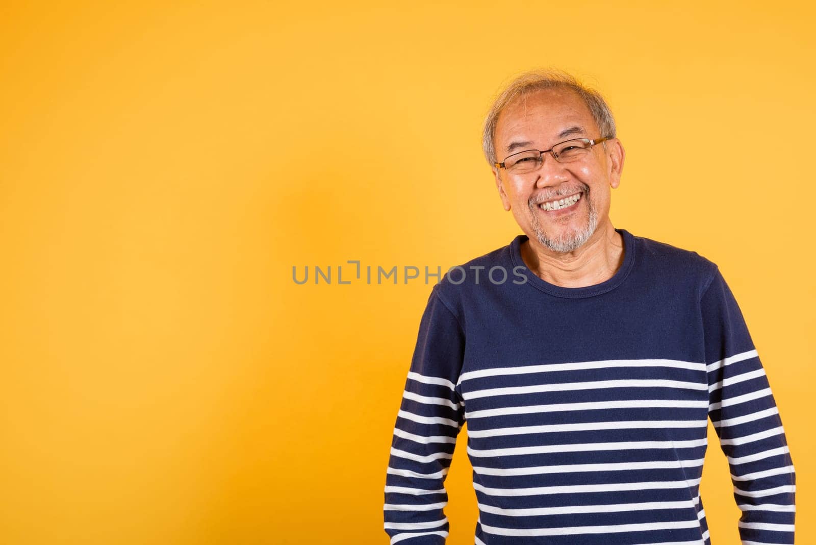 Portrait Asian smiling old man with glasses is smiling and wearing a blue striped sweater studio shot isolated yellow background. The image has a cheerful and positive mood, Senior man with grey hair