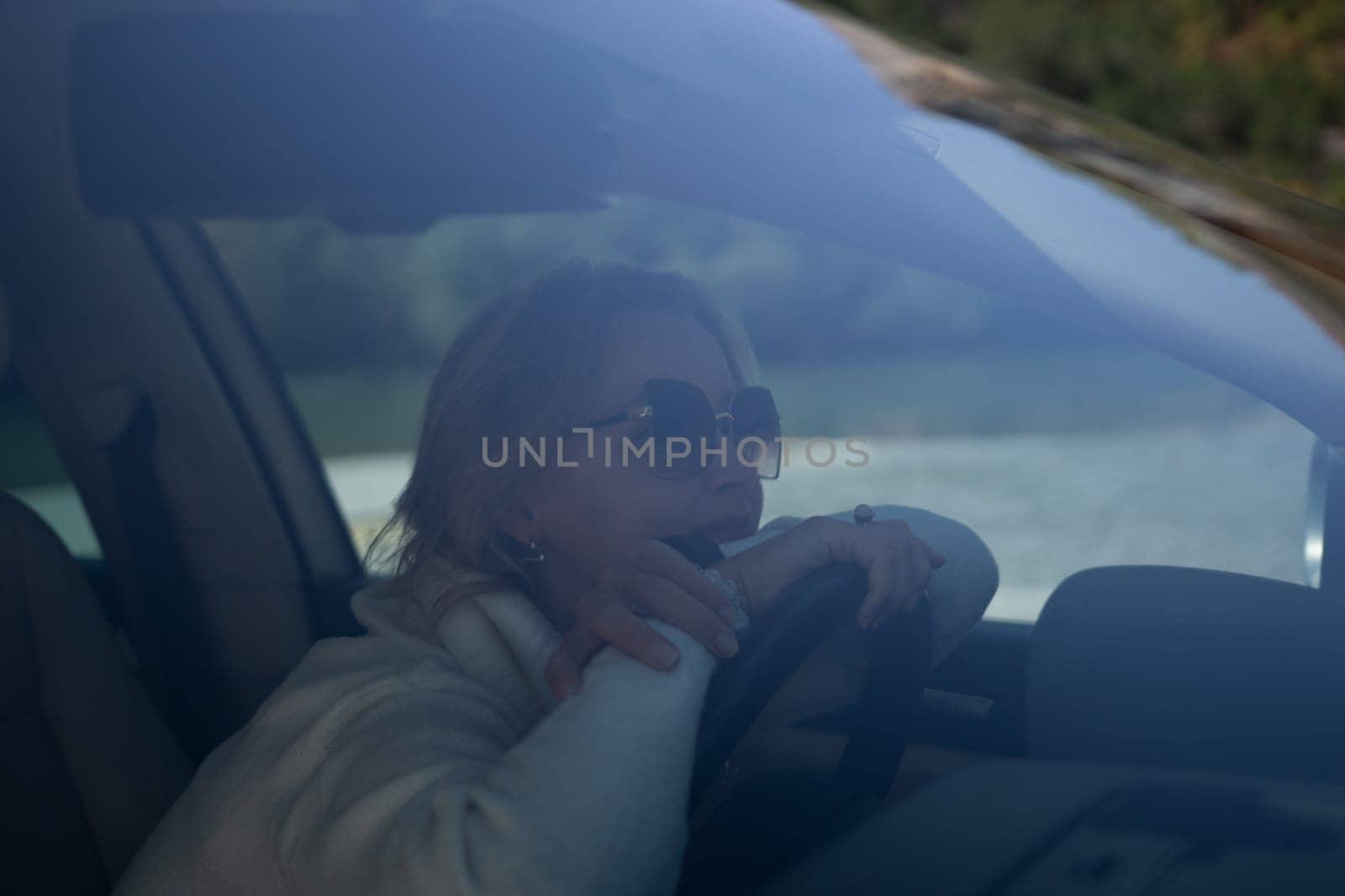 A blonde woman in a white sweater and jeans is driving. Happy woman sitting in a car with a white interior. by Matiunina