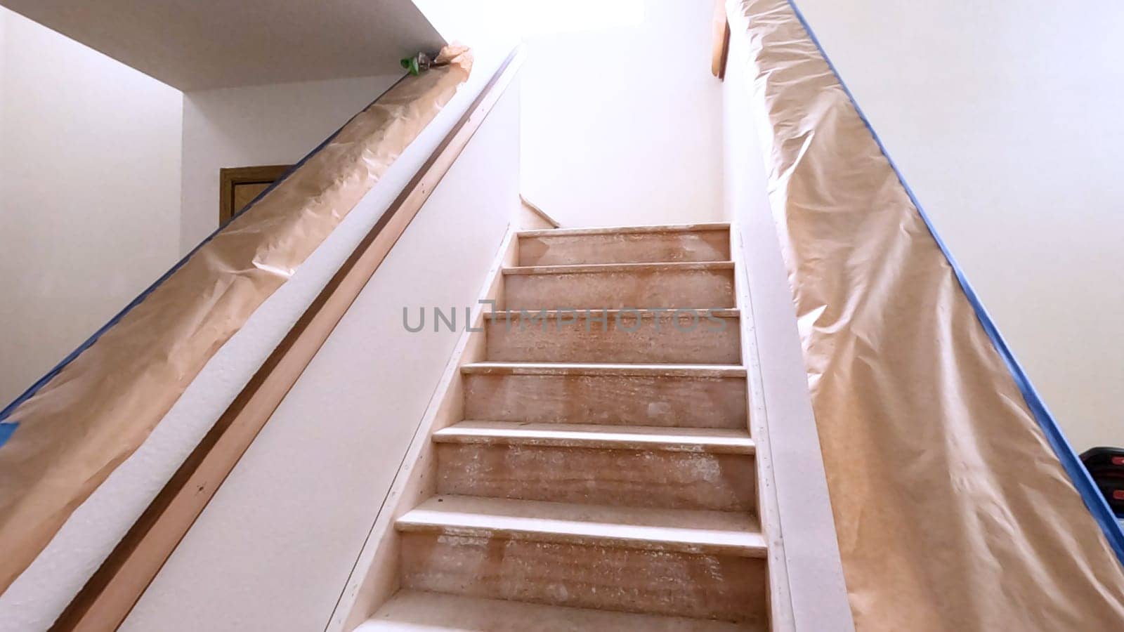 A staircase in a home undergoing renovation, featuring protective coverings and masking tape to safeguard surfaces. The area is prepared for painting or further construction work, highlighting a common home improvement project.