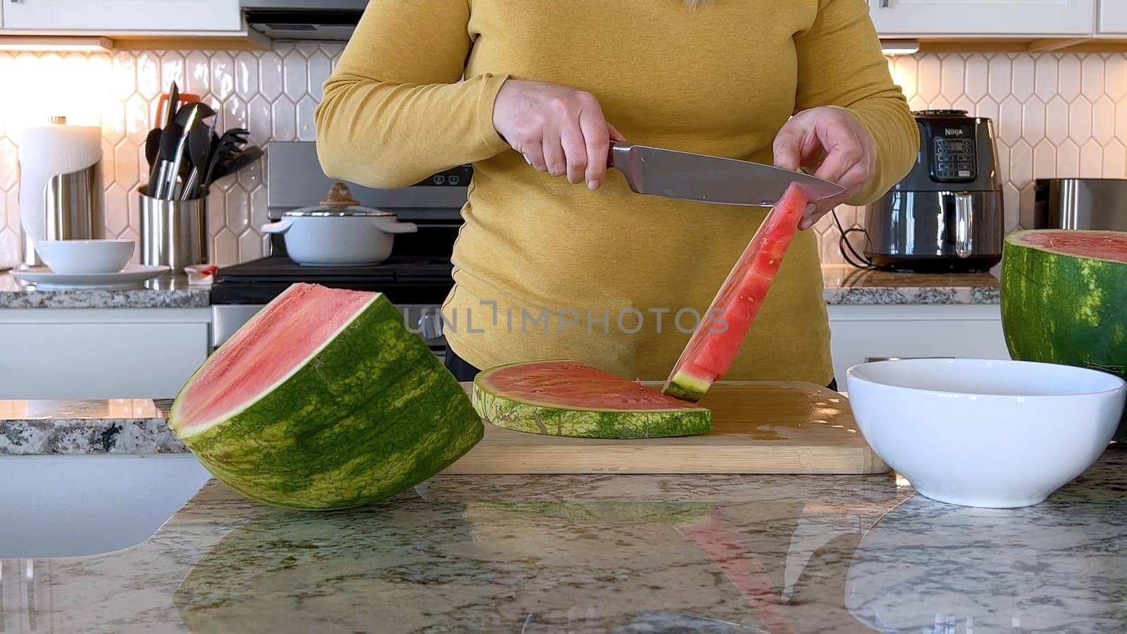 Woman Slicing Watermelon in a Modern Kitchen by arinahabich