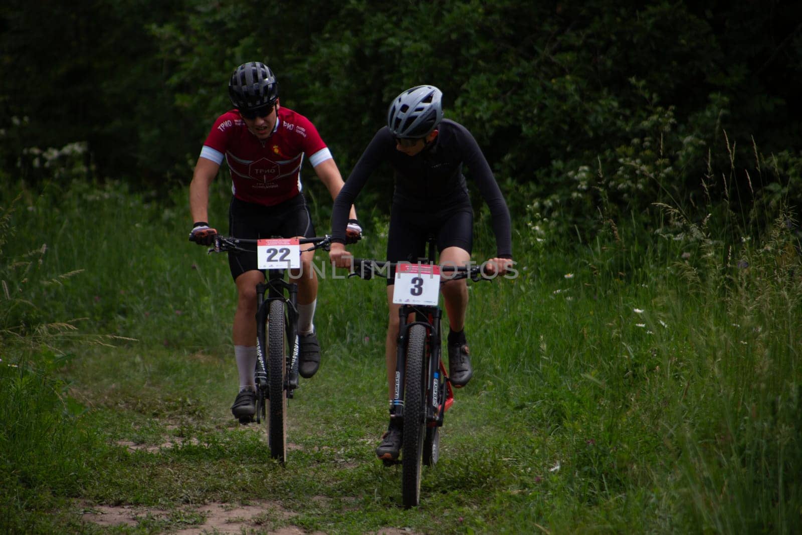 Kursk, Russia, June 15, 2024: Boys on cross country bikes fight for position on straight line on long grass trail, mountain bike competition