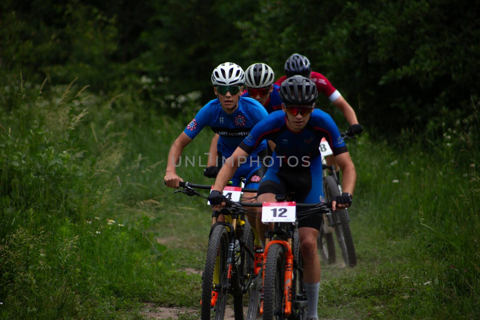 Kursk, Russia, June 15, 2024: Row of athletes at off-road cycling competition fight for position, line of mountain bike racers in forest