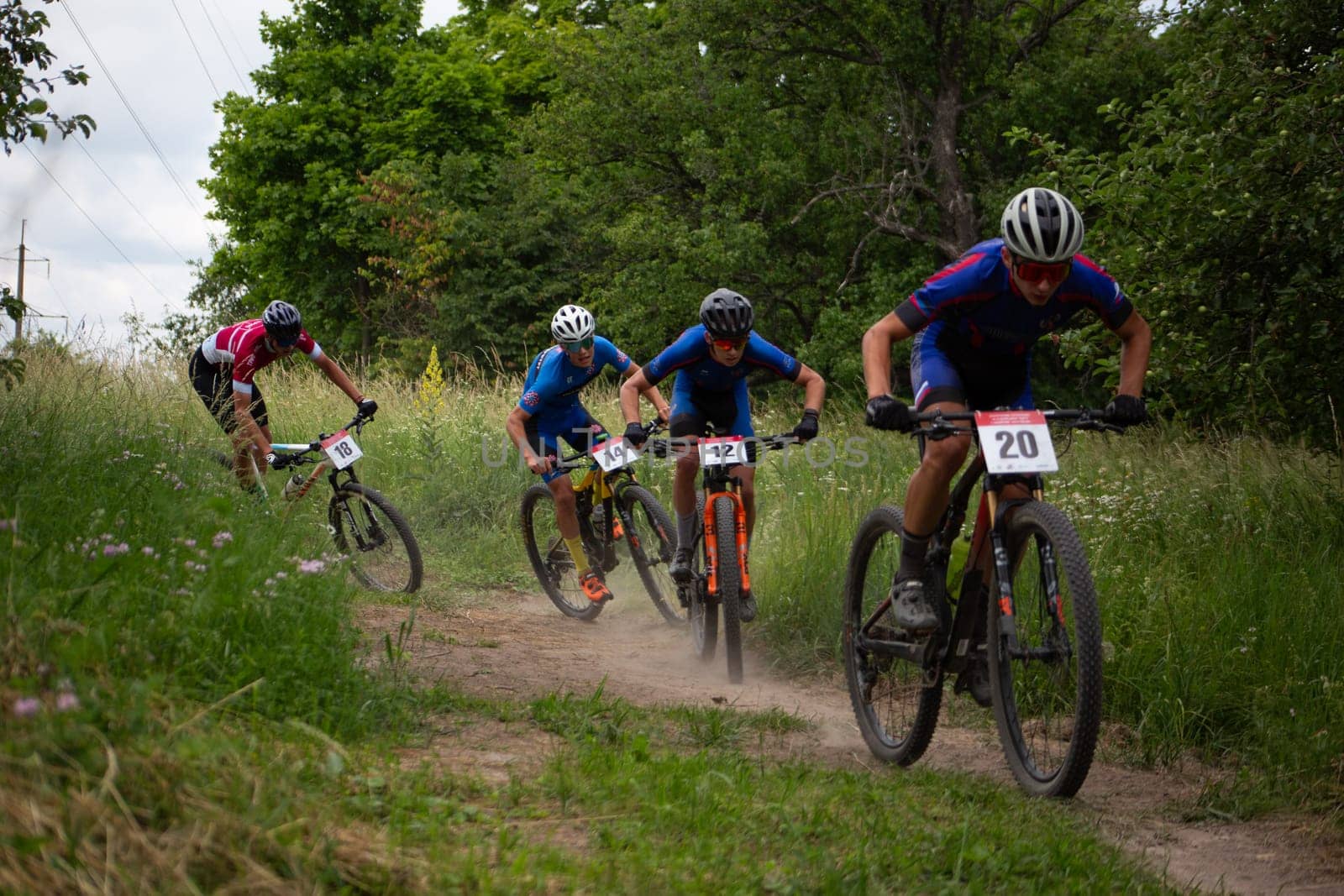 Kursk, Russia, June 15, 2024: Young athletes quickly ride along dust path along the forest at cycling competition, fighting for position in mountain bike tournament