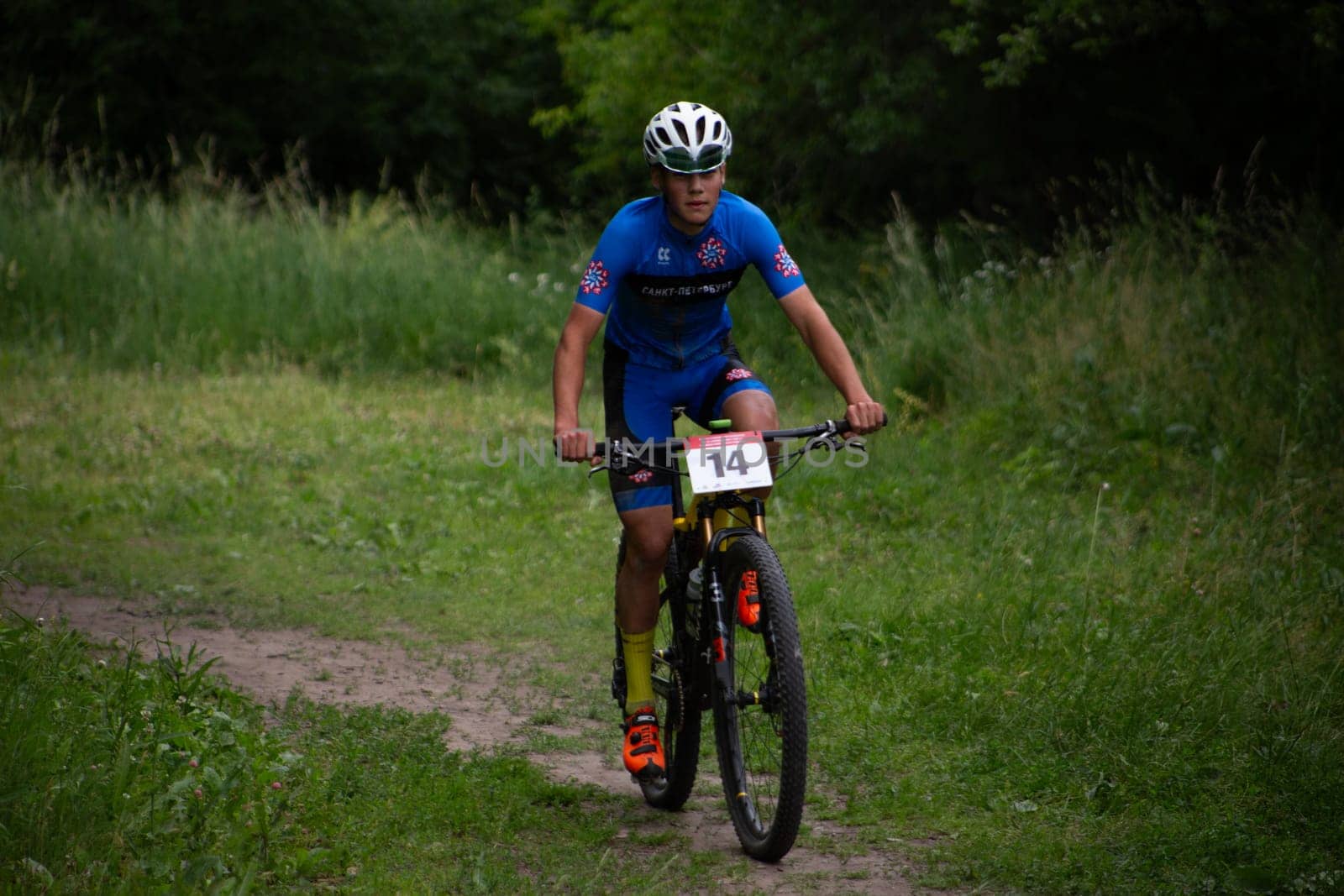 Kursk, Russia, June 15, 2024: Cyclist walks along path in forest at mountain bike competition, young athlete rides bicycle over rough terrain