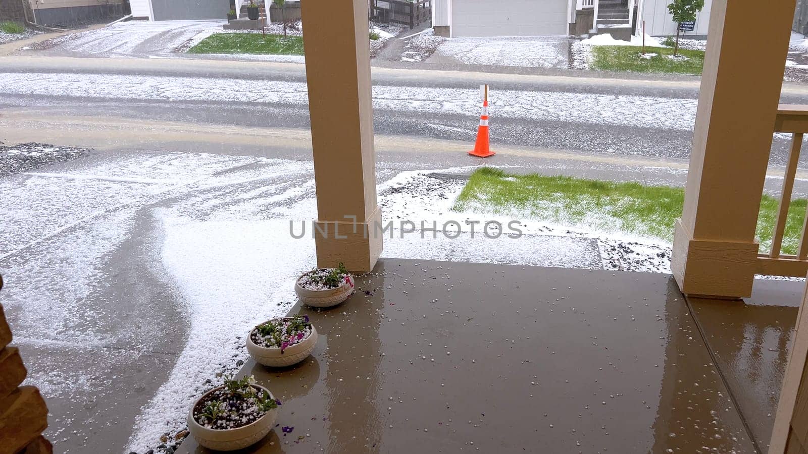 A lawn and rock garden blanketed in hail following a storm, with the green grass and small shrubs peeking through the layer of ice. The contrast between the white hail and the greenery creates a striking visual effect.