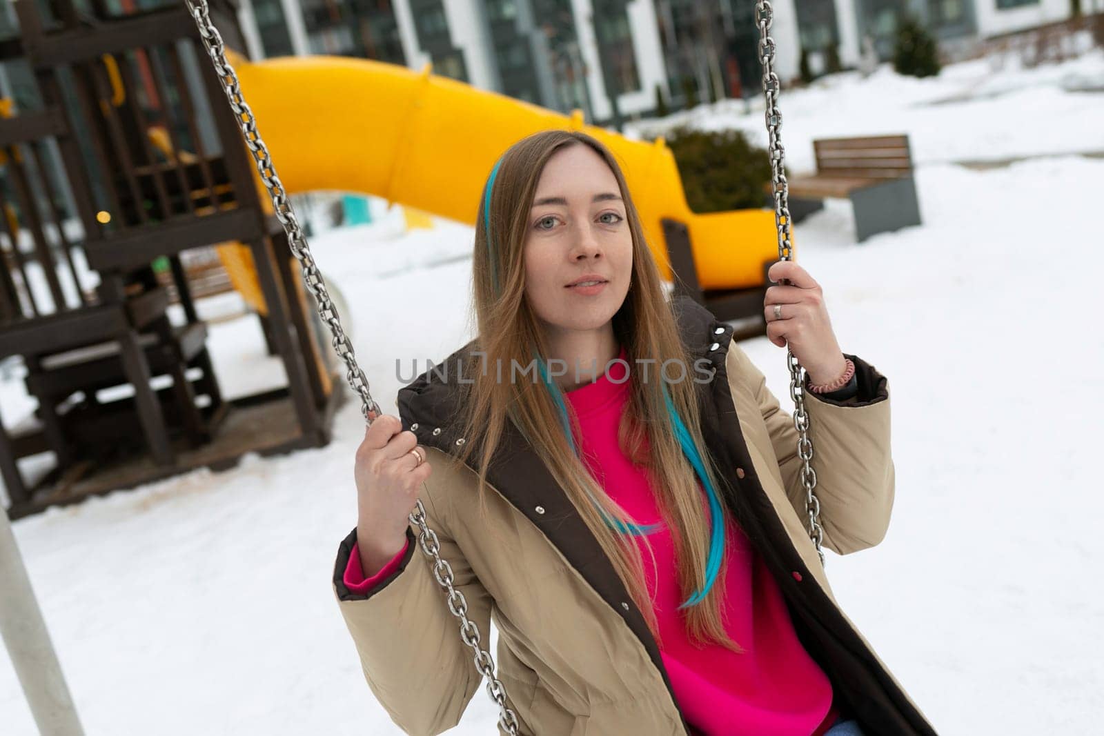 A woman is sitting on a swing covered in snow. The winter landscape surrounds her as she quietly enjoys the snowy scenery.