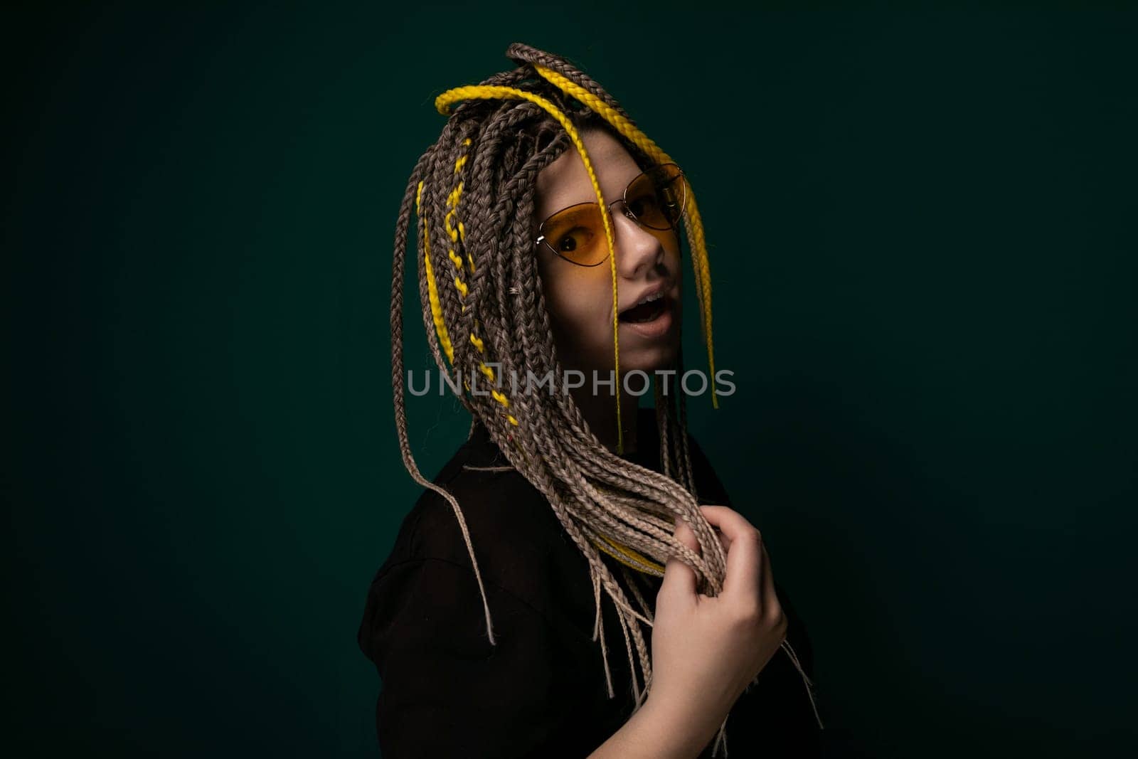 A woman with dreadlocks is standing in front of a solid green background. She is looking at the camera with a neutral expression, her hair cascading down her shoulders.