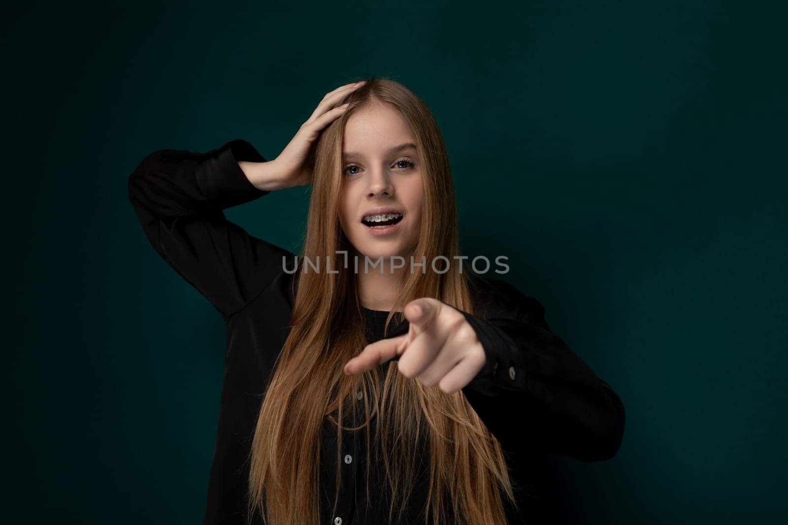 A woman with vibrant red hair is pointing directly at the camera, engaging the viewer with a confident expression. Her long red locks cascade down her shoulders, drawing attention to her gesture.