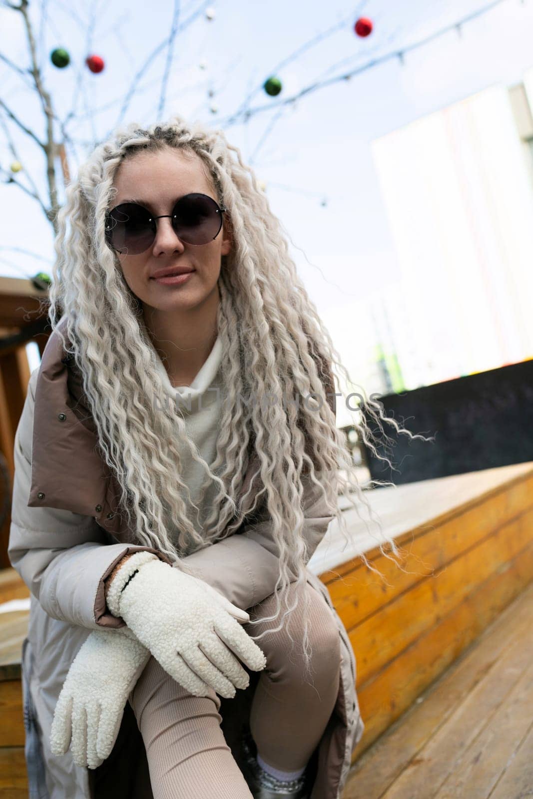 A woman with long blonde hair is sitting on a bench, looking towards the distance. Her hair cascades down her back, and she appears lost in thought.