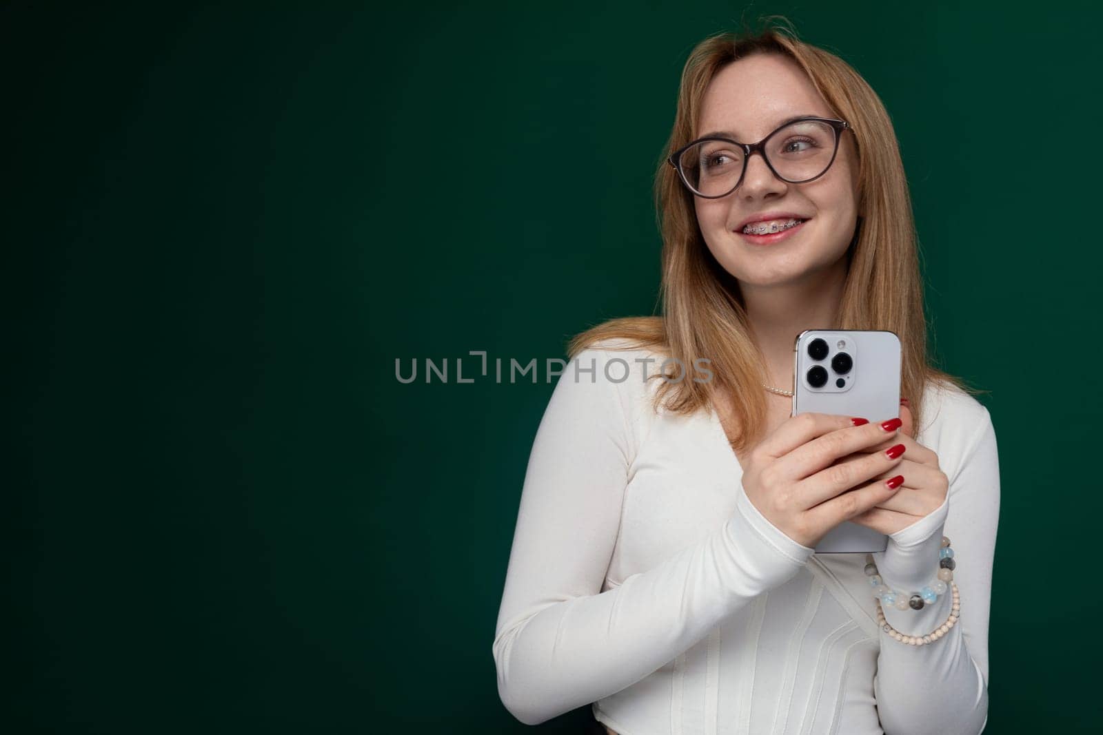 A woman wearing glasses is holding a cell phone in her hands. She appears to be focusing on the devices screen, possibly texting or browsing. The background is blurred, emphasizing her action.