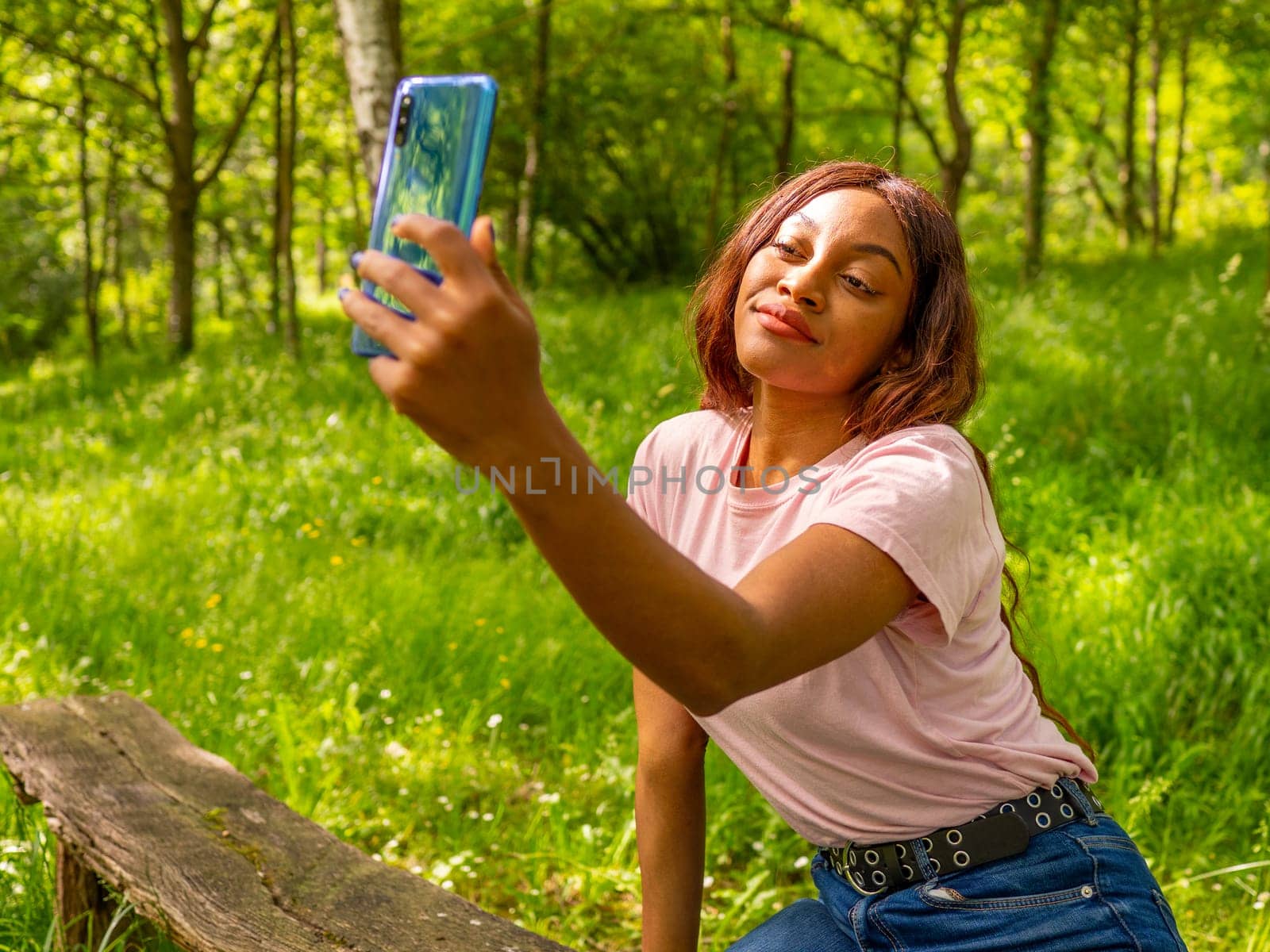 Young black woman with her phone taking selfie in a park on an October afternoon. by Ceballos