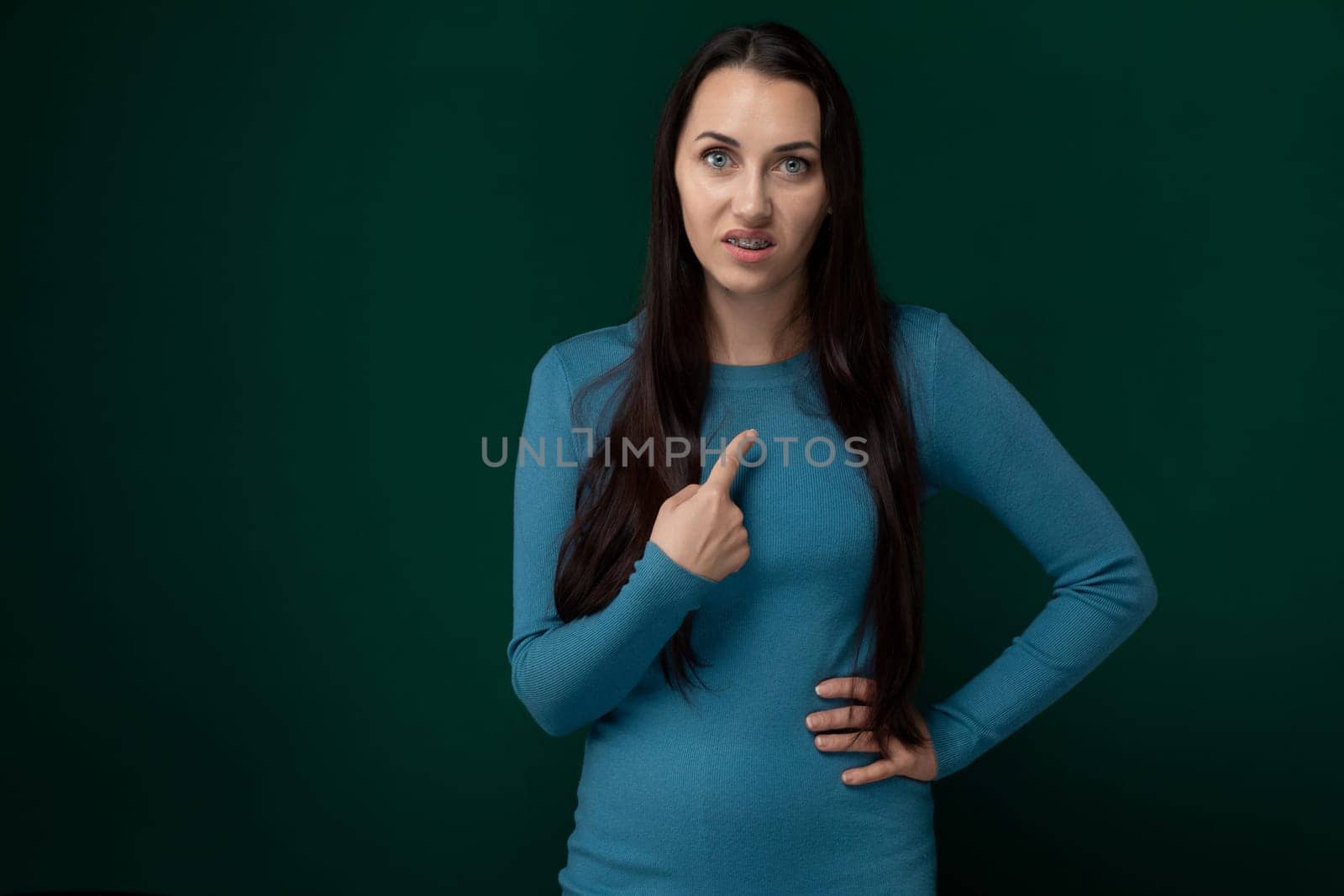 A woman with long brown hair wearing a blue shirt is smiling and giving a thumbs up gesture.