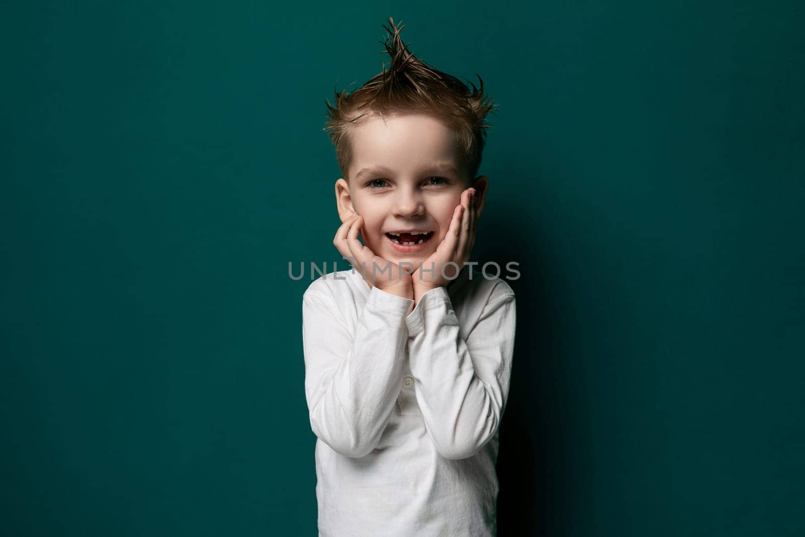 A young boy is standing upright in front of a vibrant green wall. He appears to be looking directly at the viewer, with a curious and innocent expression on his face. The boy is wearing casual clothing and does not seem to be interacting with anyone or anything else in the scene.