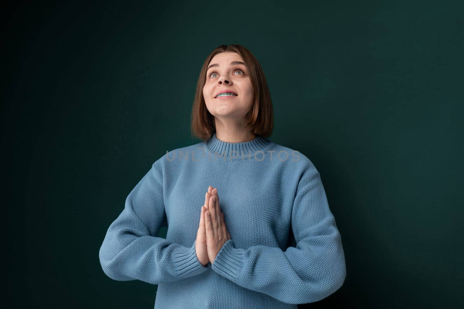 A woman is standing in front of a green wall, looking directly at the camera. She is wearing casual clothing and appears to be posing for a photo.