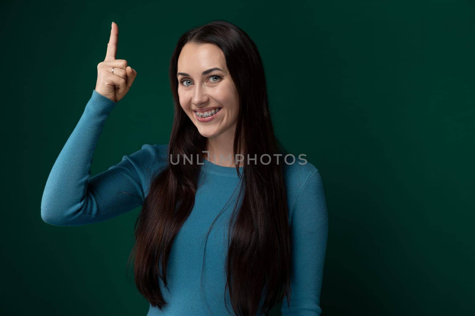 A woman with long black hair is standing and pointing to the side. She appears focused and engaged as she gestures towards something off-camera. Her hair cascades down her back, adding to the visual appeal of the scene.