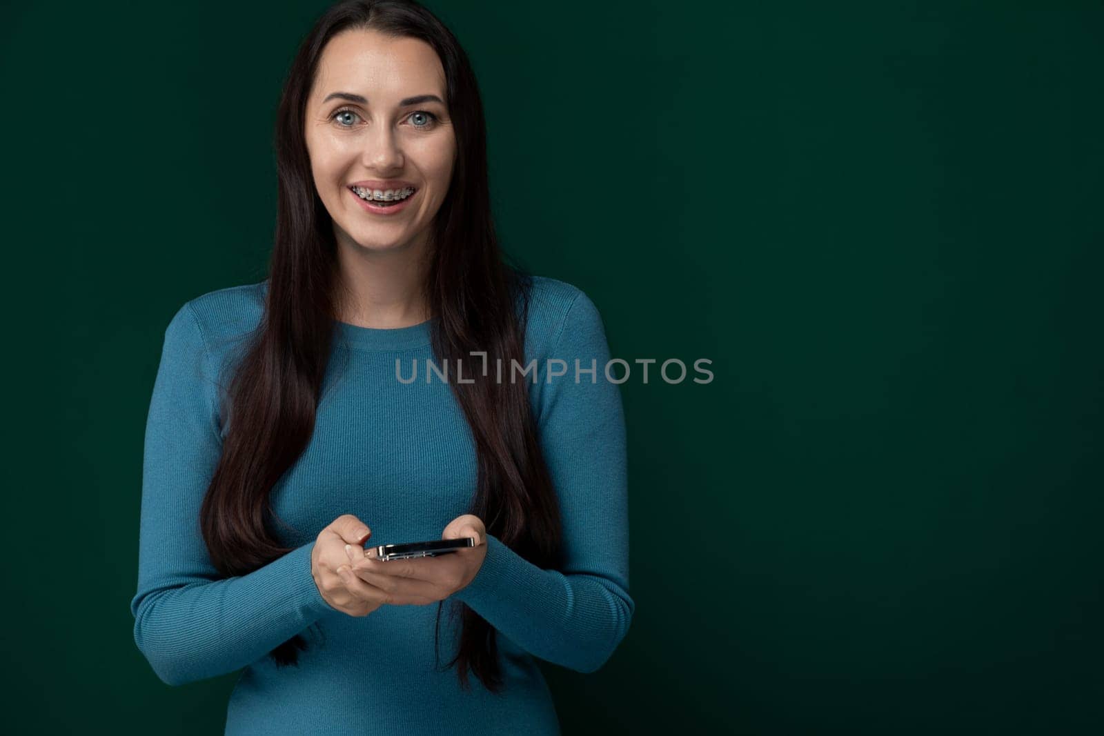 A woman is seen holding a cell phone in her hands, focusing on the screen. She appears engaged with the device, possibly texting, calling, or browsing. The background is neutral, keeping the spotlight on the woman and her phone.
