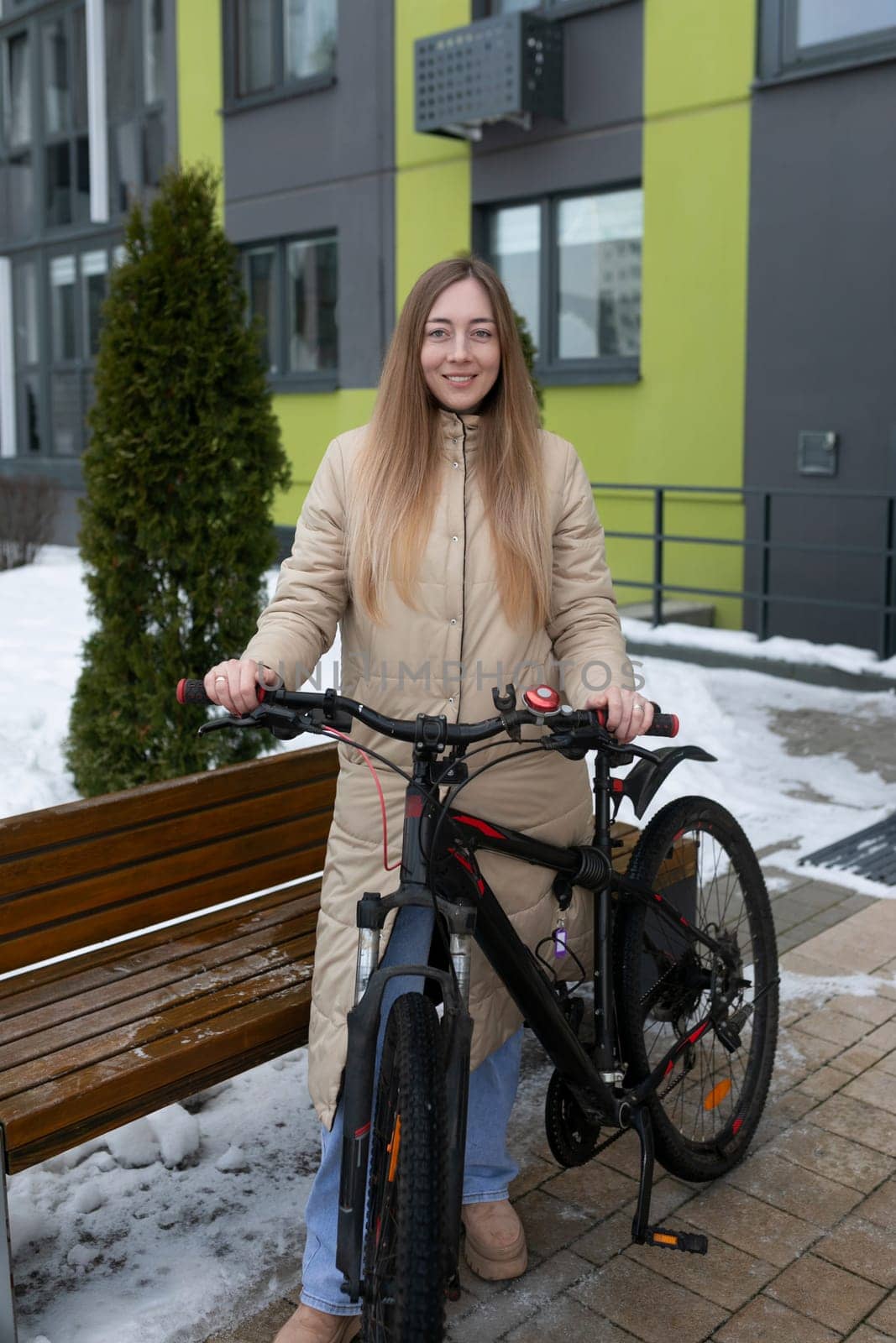A woman wearing winter clothing is standing next to a bicycle on a snowy ground.