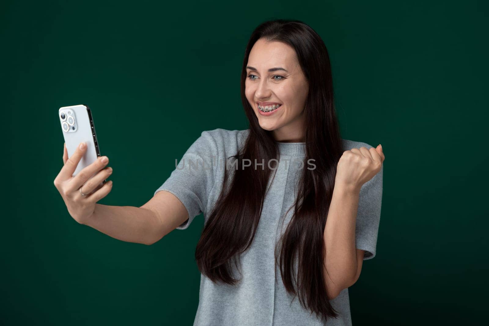 A woman holding a cell phone, posing for a selfie. She is smiling and looking at the phones screen while taking the picture.