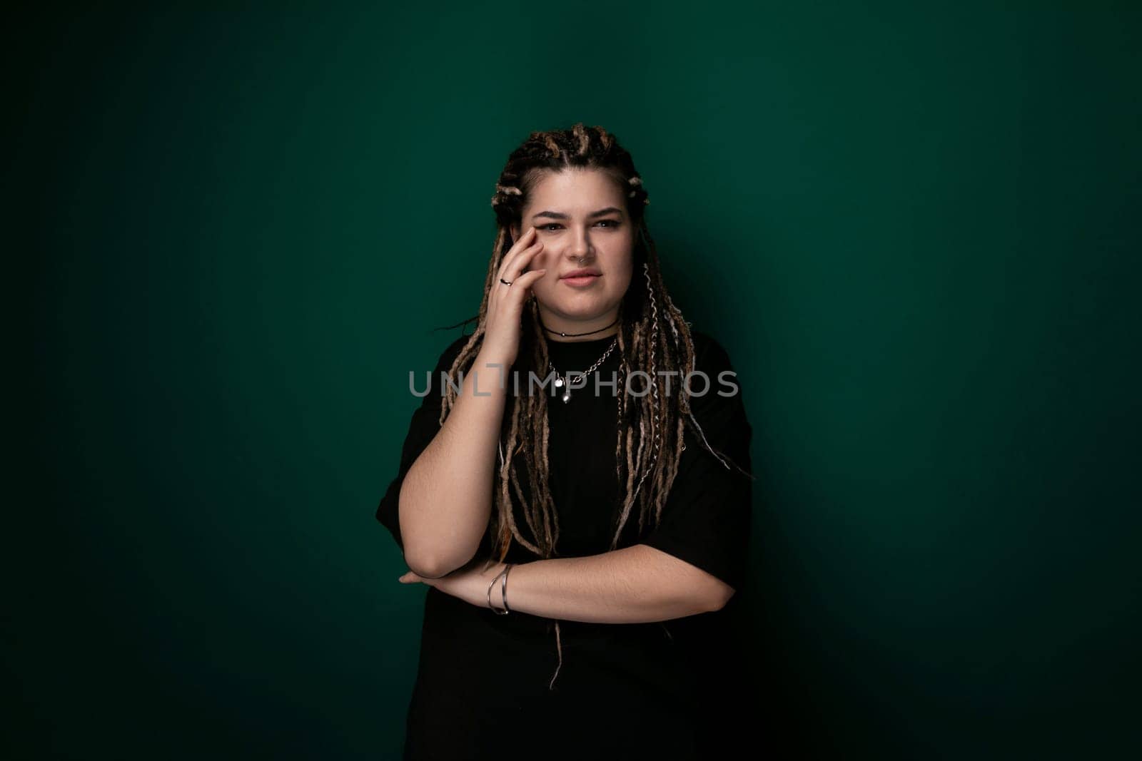 A woman with dreadlocks is seen standing against a vibrant green wall. She appears confident and stylish as she poses for the camera.