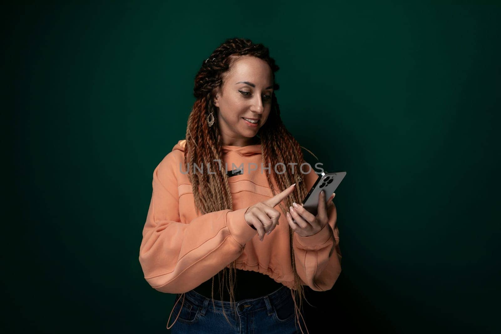 A woman with dreadlocks is using her cell phone. She is focused on the screen, tapping and scrolling. Her hair is styled in long, twisted dreadlocks. She appears engaged in whatever she is doing on the phone.