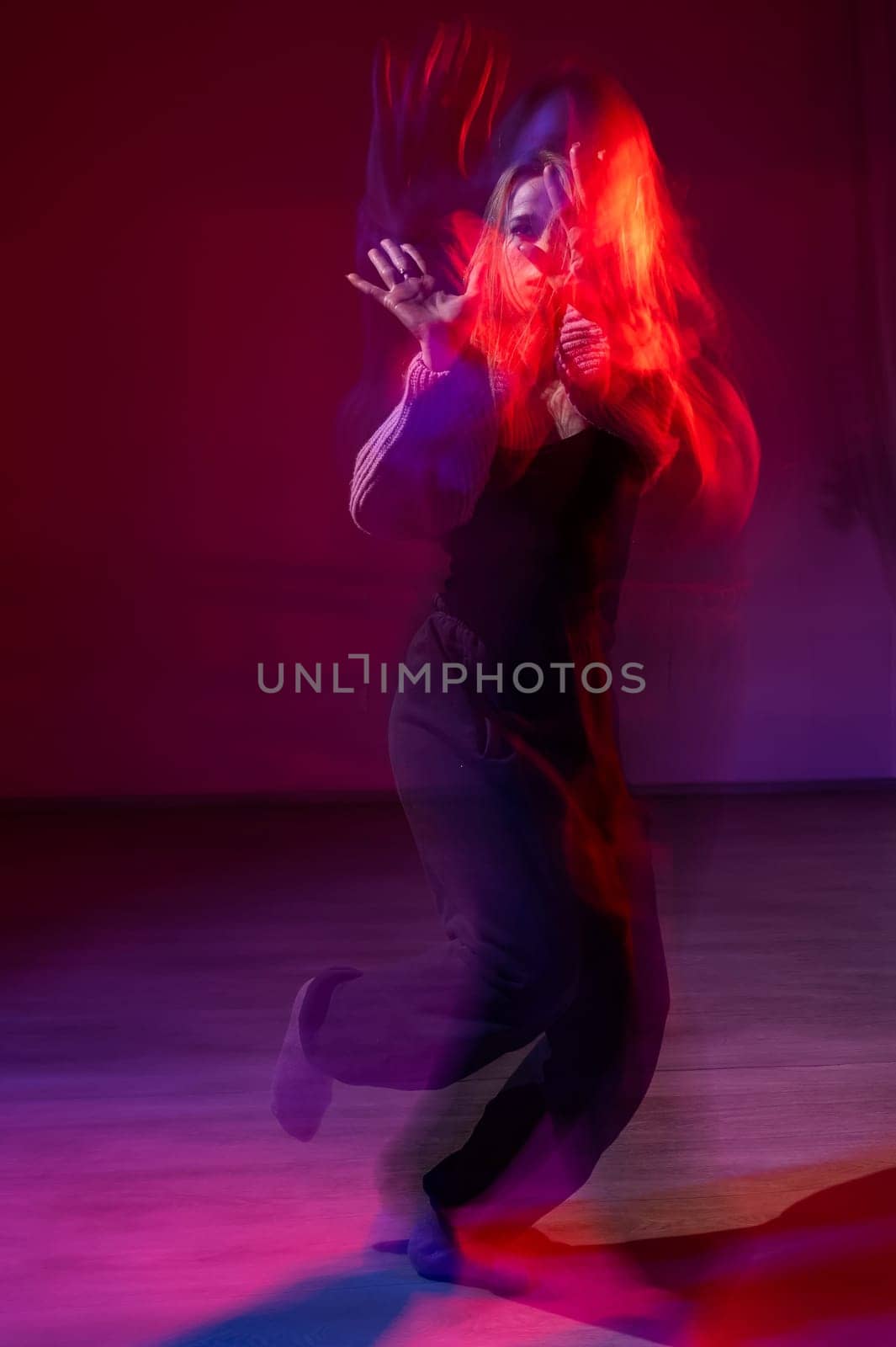 A young woman dances contemporary dances in blue and red light. Long exposure. Vertical photo