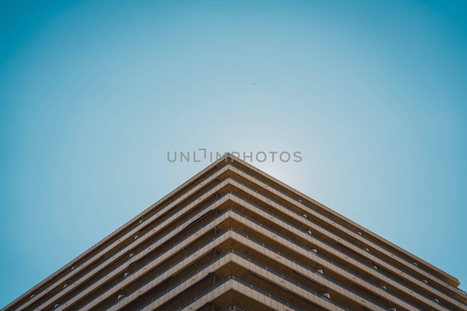 Unique perspective of a building s corner facade with balconies, set against a clear sky. Sant Antoni beach, Cullera, Spain