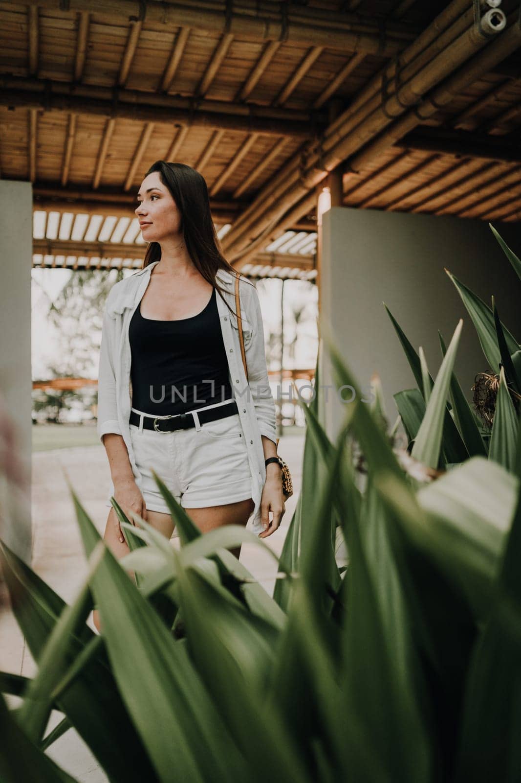 A woman walks through a bamboo-covered pathway. The setting features lush plants and a serene atmosphere, emphasizing a connection with nature and a relaxed, contemplative mood.