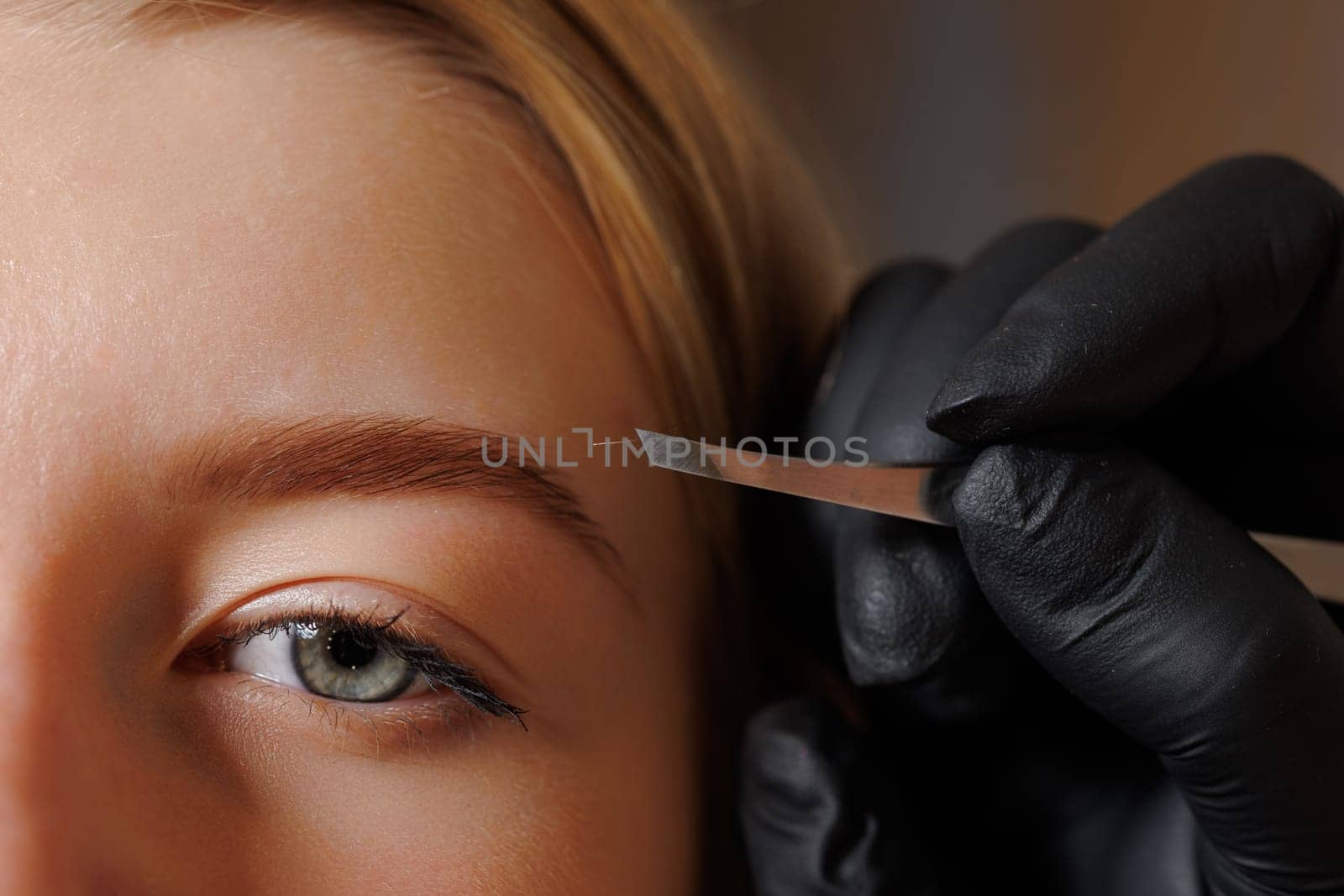 Master eyebrow artist makes eyebrow correction to a girl in a beauty salon, close-up of eyebrow care, self-care concept