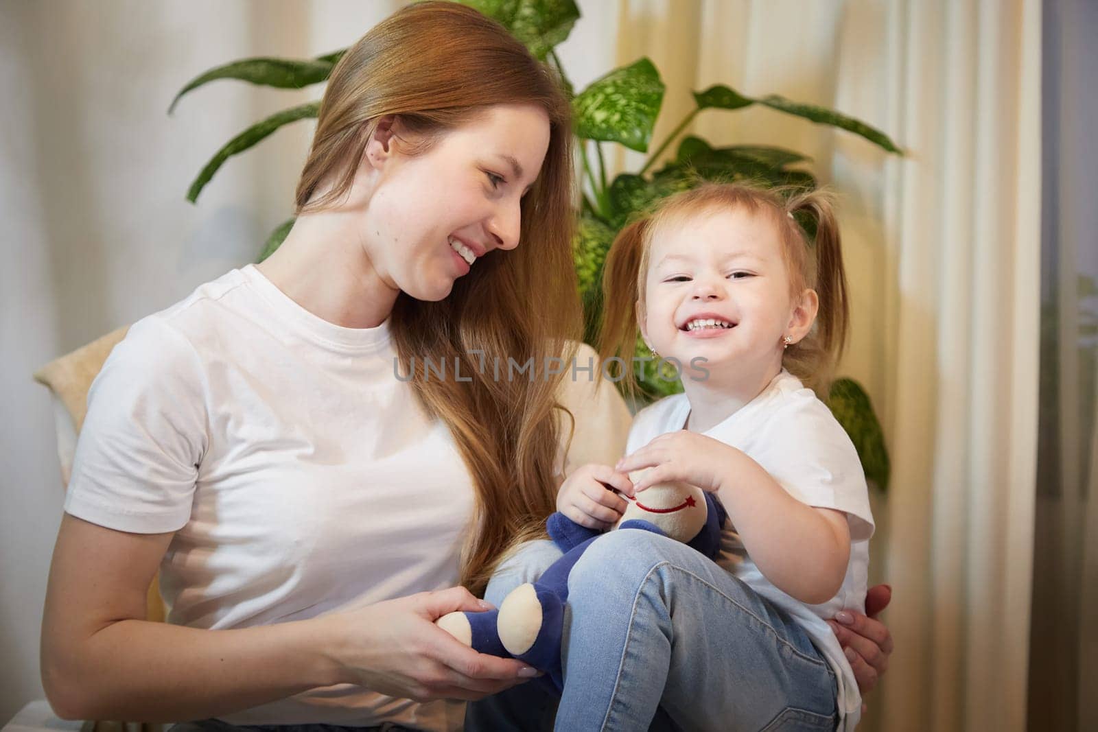 Happy loving family. Mother and daughter child girl playing and hugging in living room with wicker chair