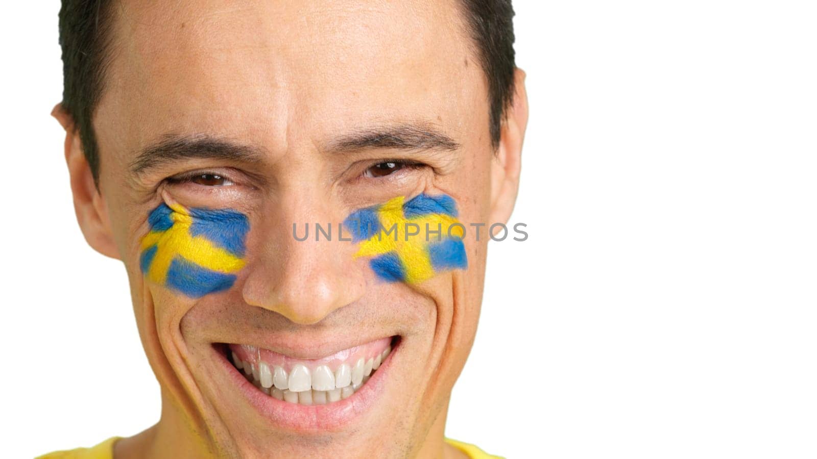 Close up of a caucasian man with a swedish flag painted on the face smiling at camera