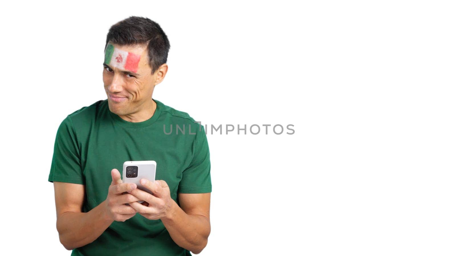 Mexican supporter with the flag of Mexico painted on his face, looking at his mobile phone smiling