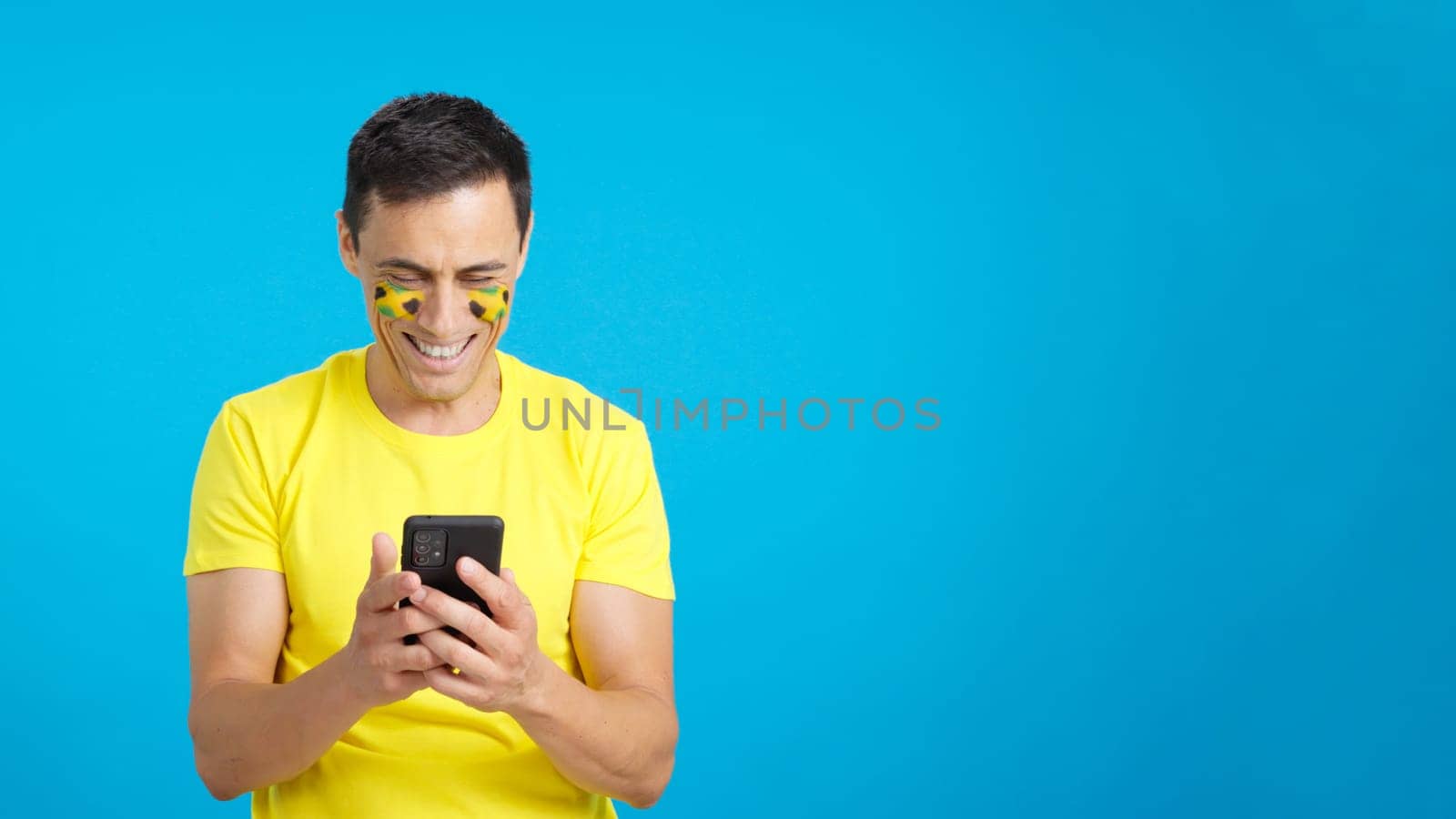 Jamaican supporter with the flag of Jamaica painted on his face, looking at his mobile phone smiling