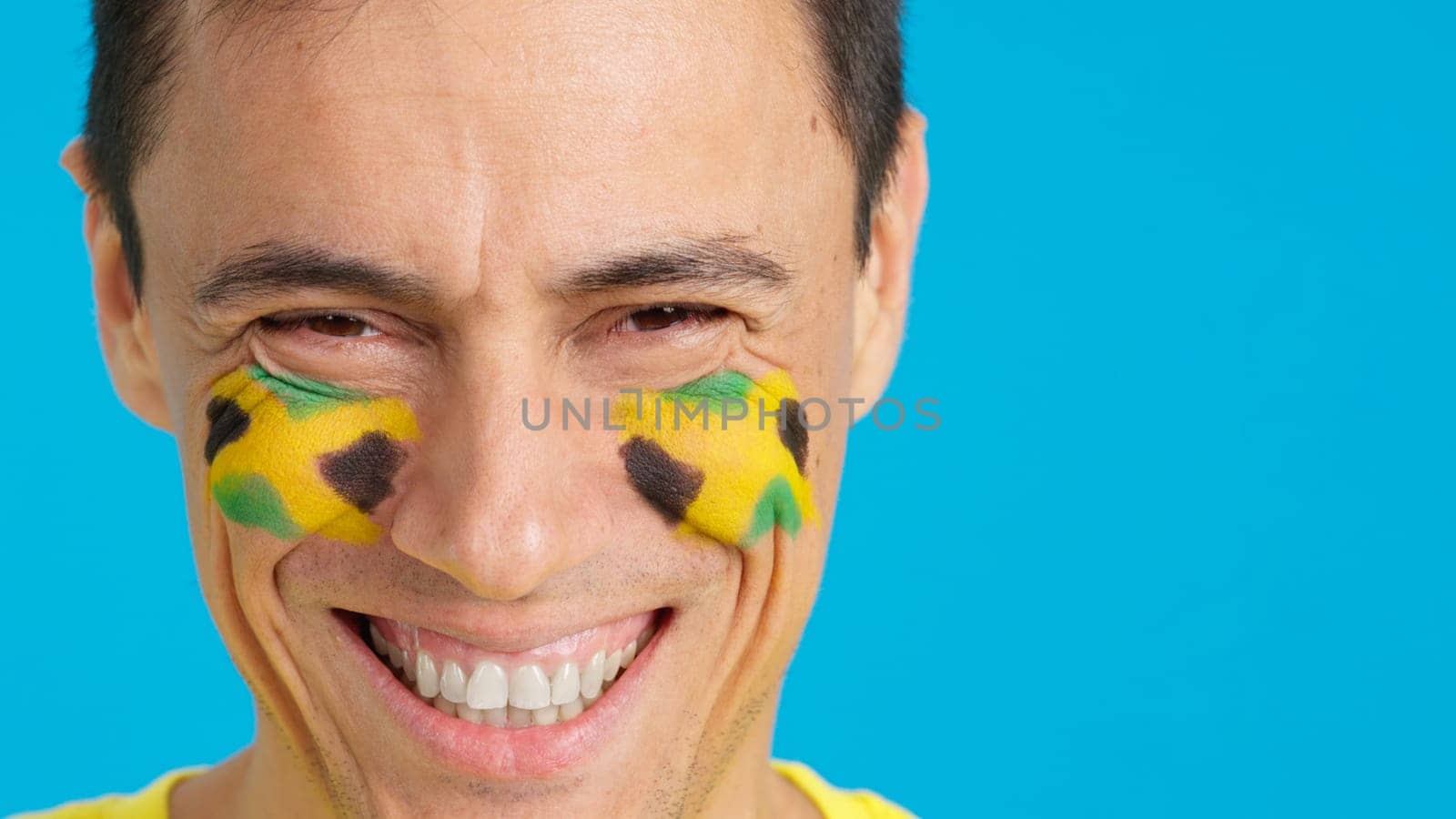 Close up of a man with a jamaican flag painted on the face smiling at camera