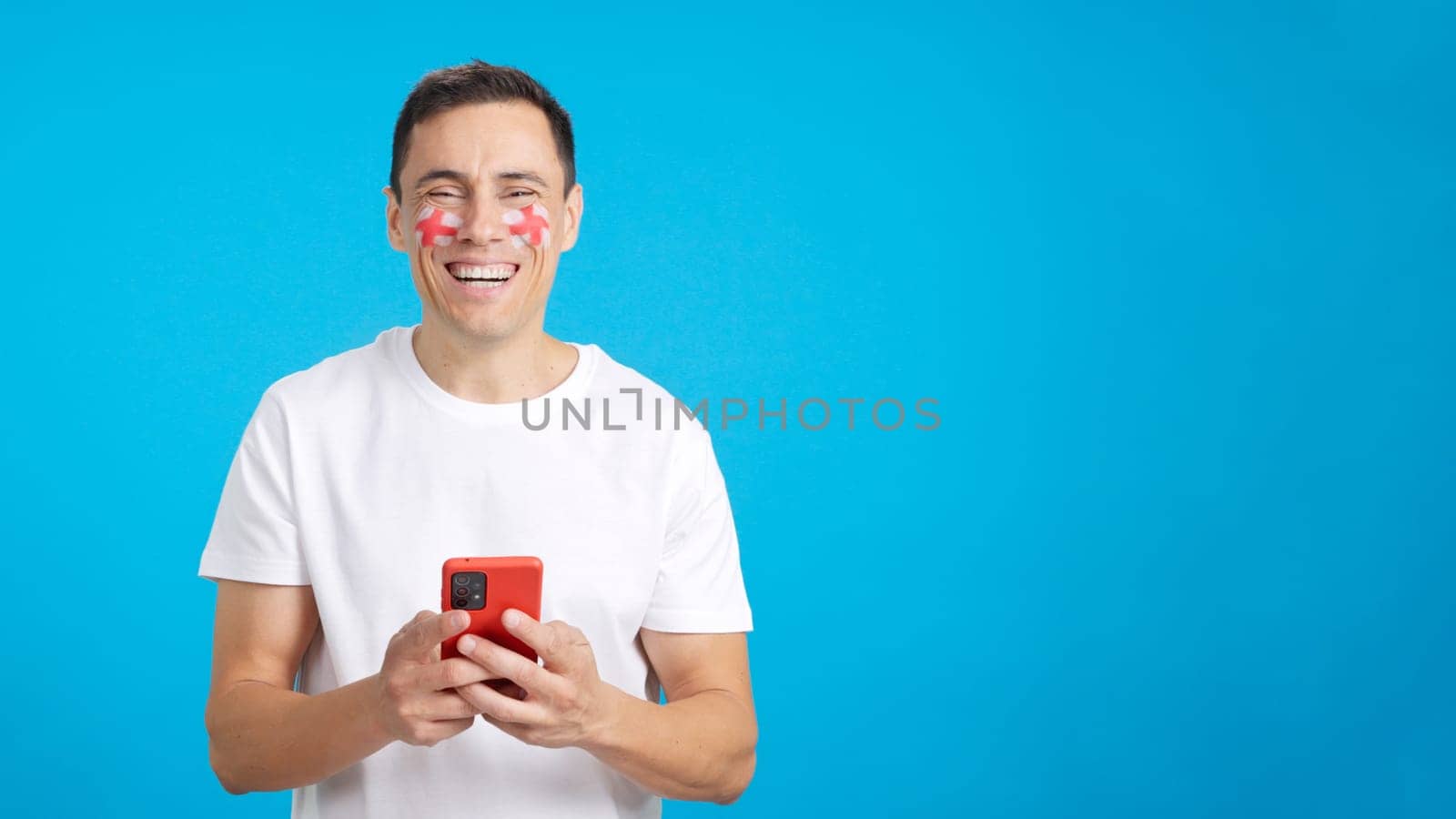 English man with the flag of England painted on his face, looking at his mobile phone smiling and showing it to the camera with the screen in chroma key.