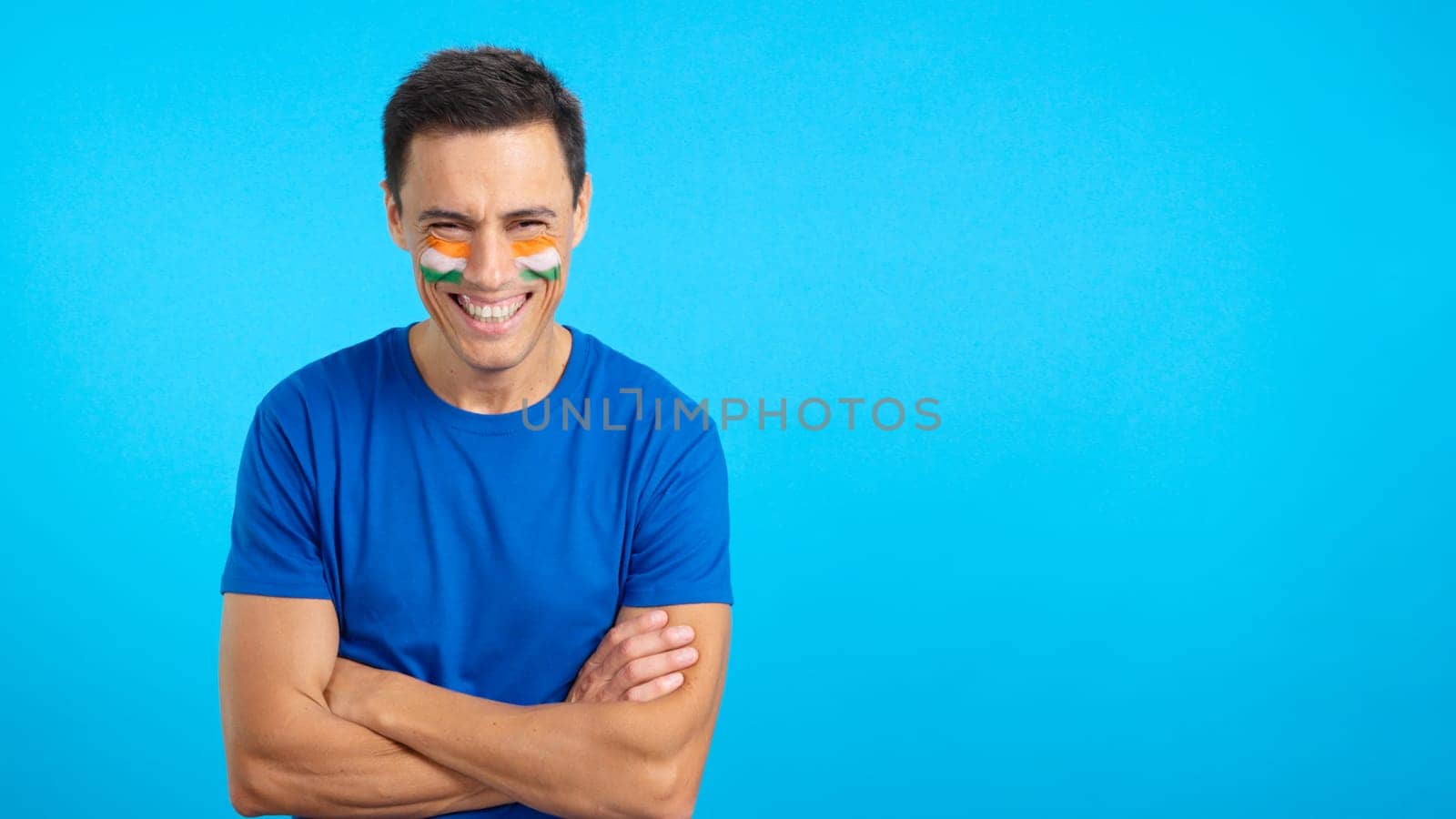 Man standing with indian flag painted on face smiling with arms crossed