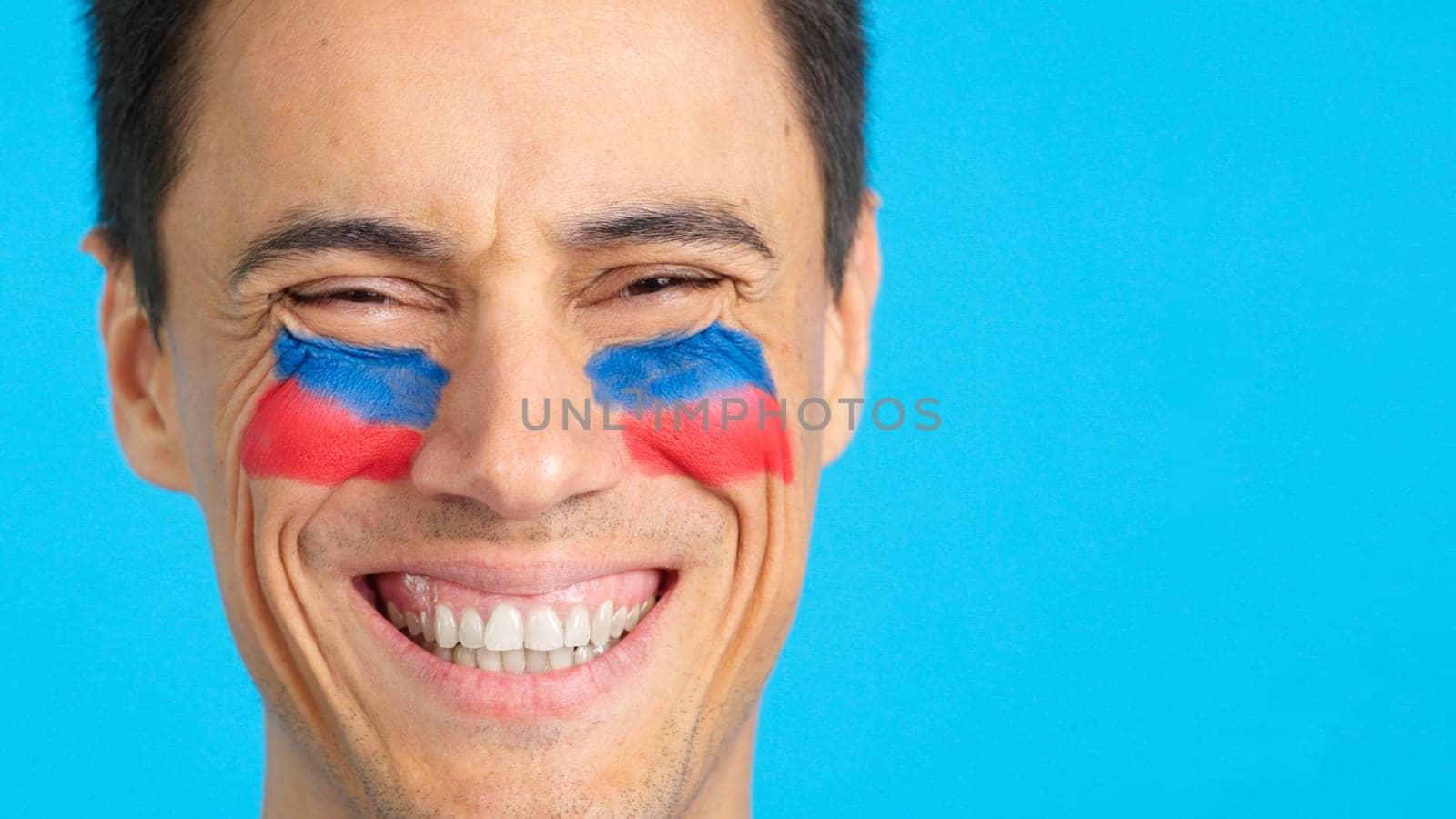 Close up of a man with a haitian flag painted on the face smiling at camera