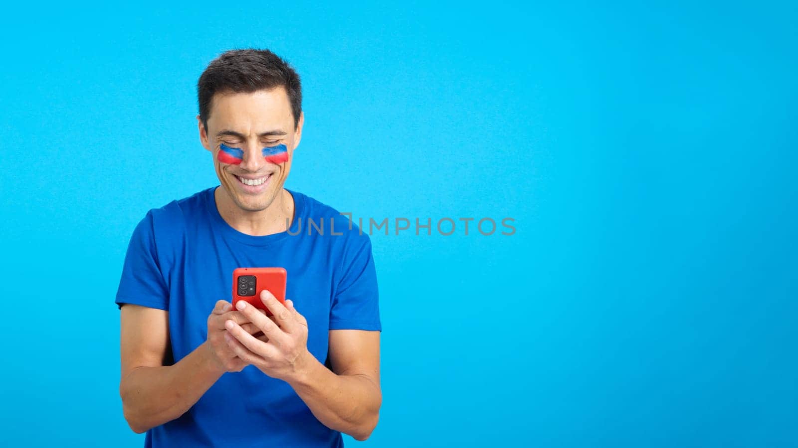 Haitian supporter with the flag of Haiti painted on his face, looking at his mobile phone smiling