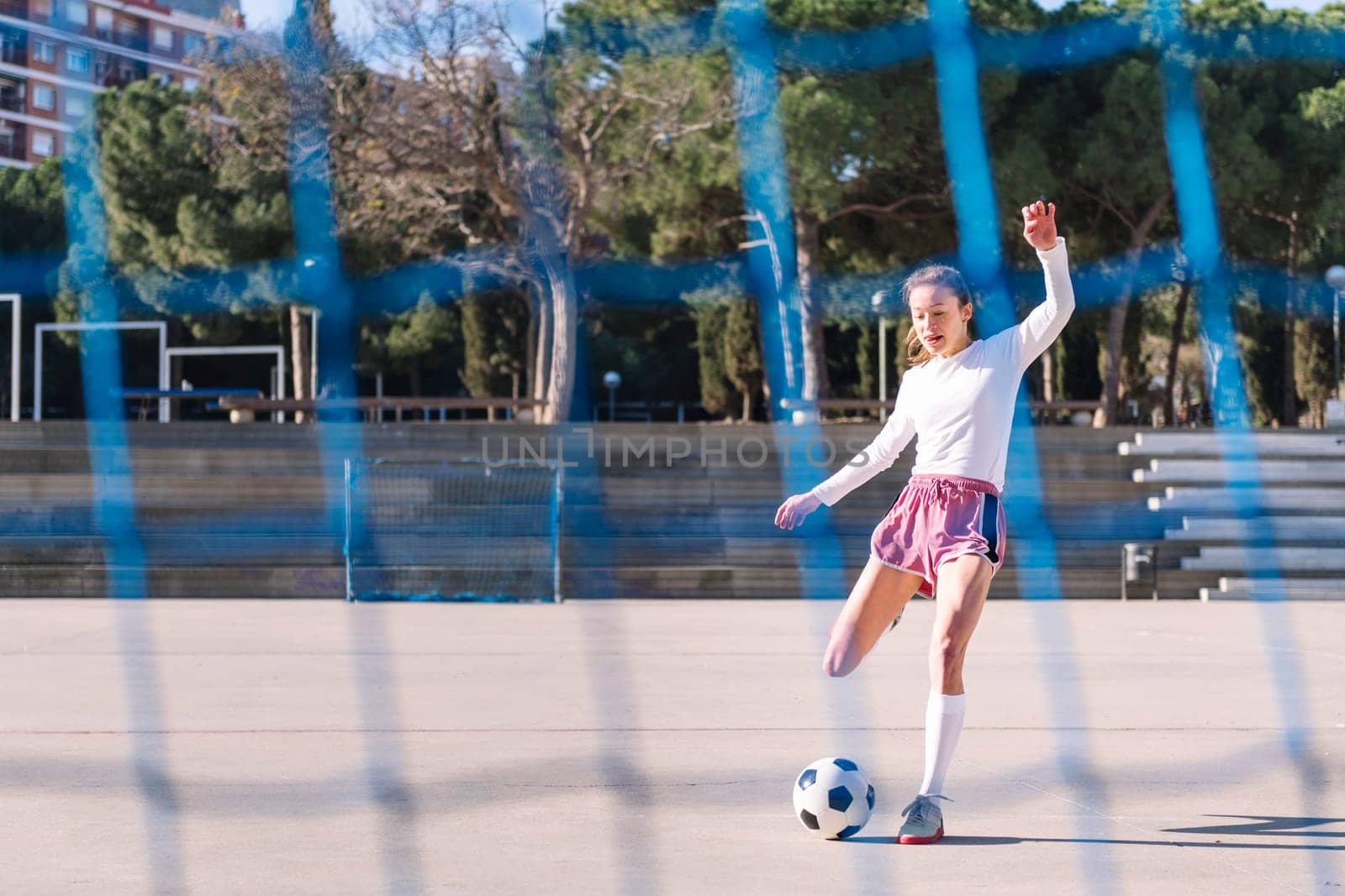 female football player kicking a soccer ball into the goal on an urban field, concept of sport and active lifestyle, copy space for text